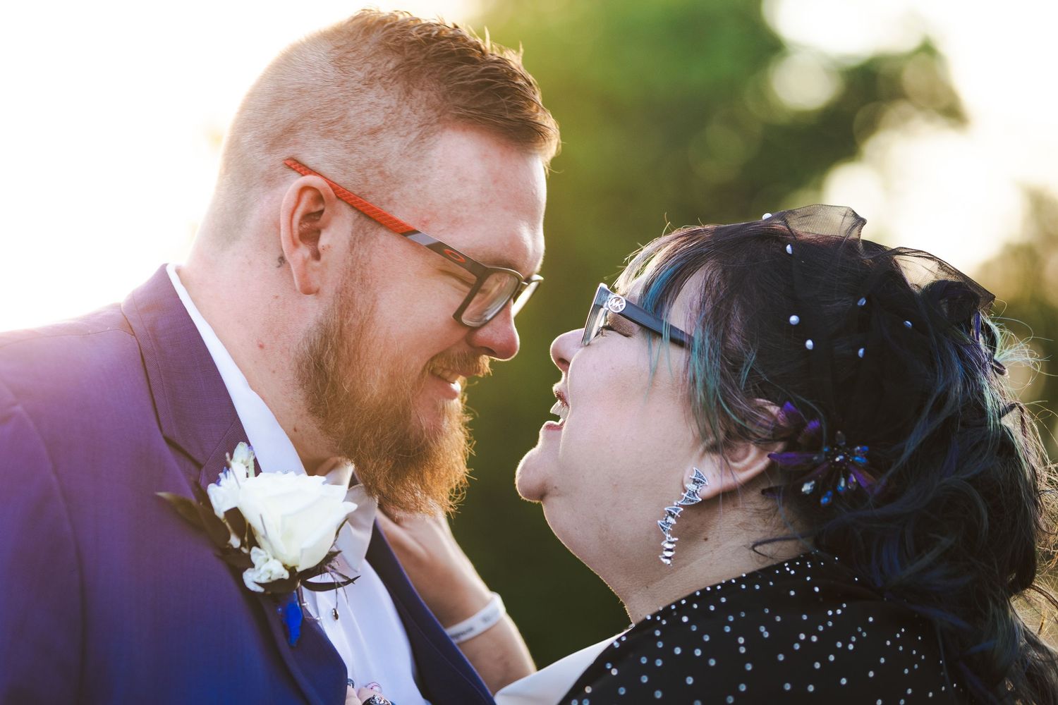 A romantic moment between a couple in formal wear against a sunlit garden backdrop.