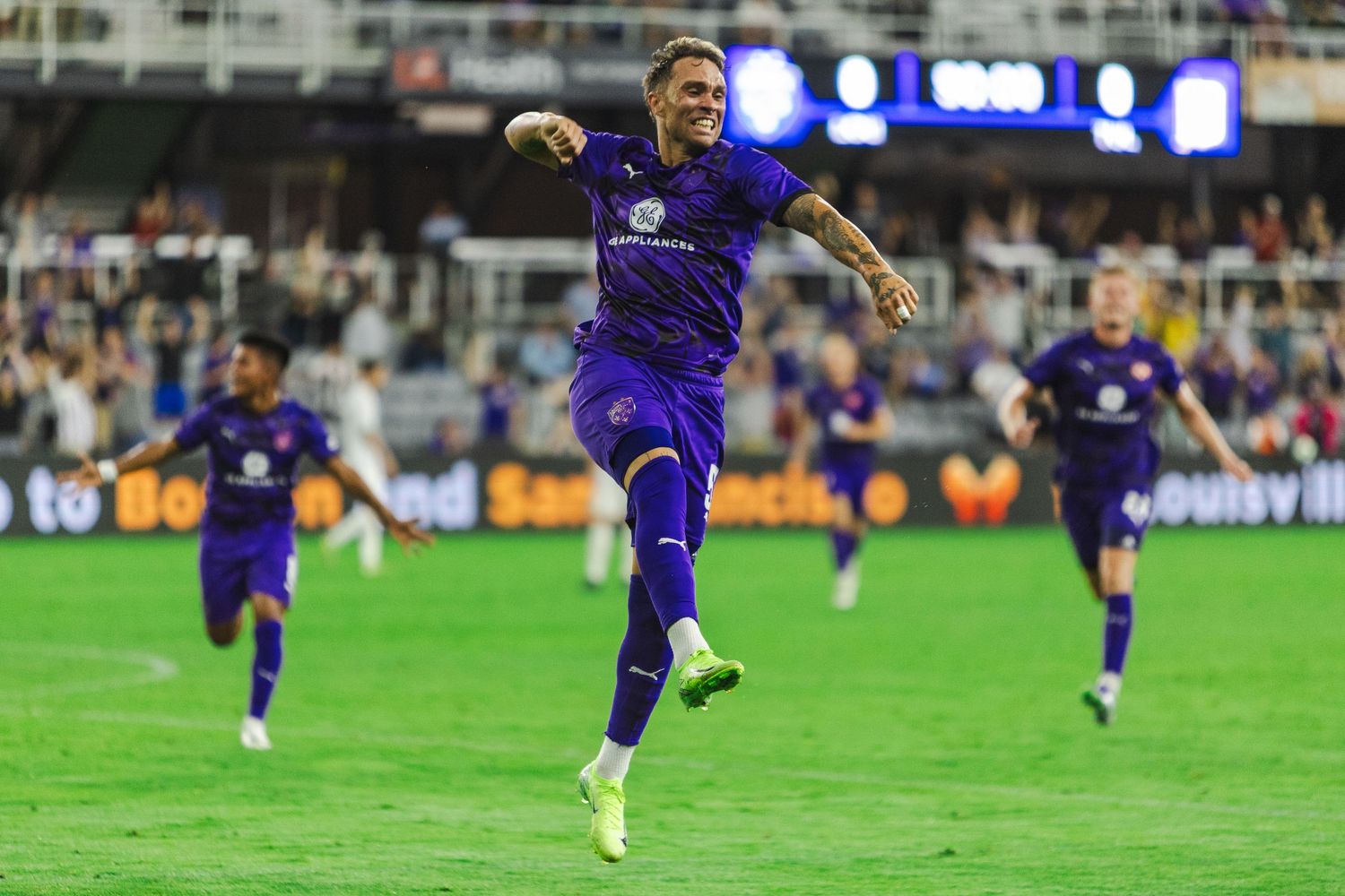 Soccer player in purple uniform dribbles ball down field during nighttime match at stadium.