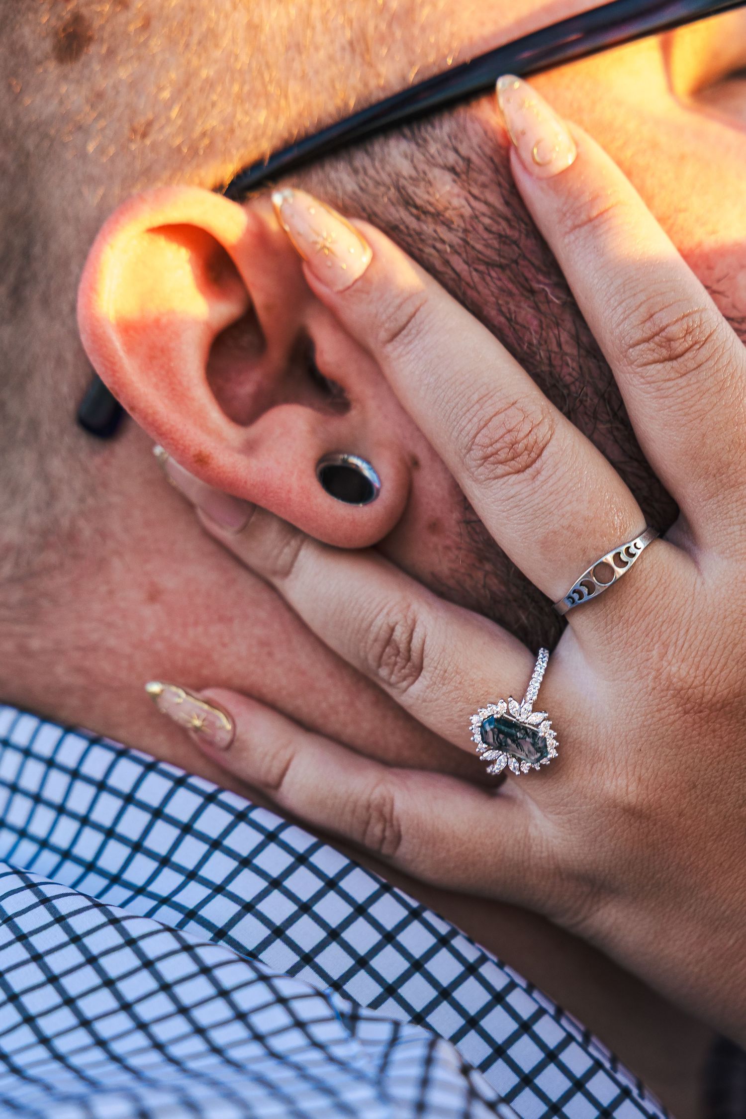 Close-up of a woman's hand with an engagement ring and manicured nails resting on a man's face near his ear.