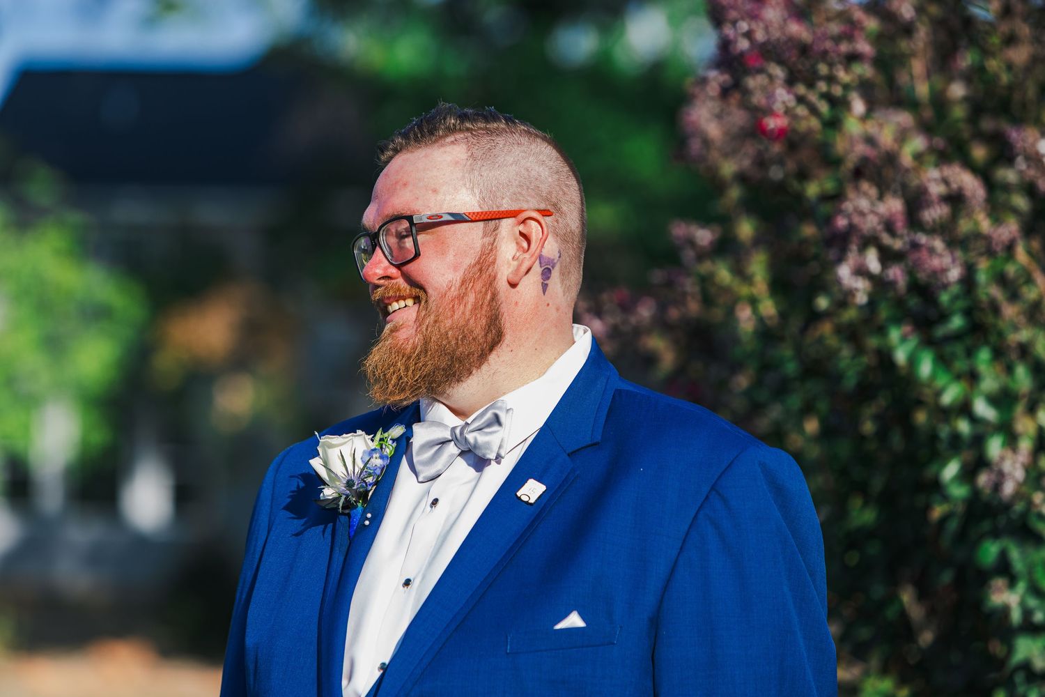 A couple in formal attire share an intimate moment outdoors with blurred greenery in the background.