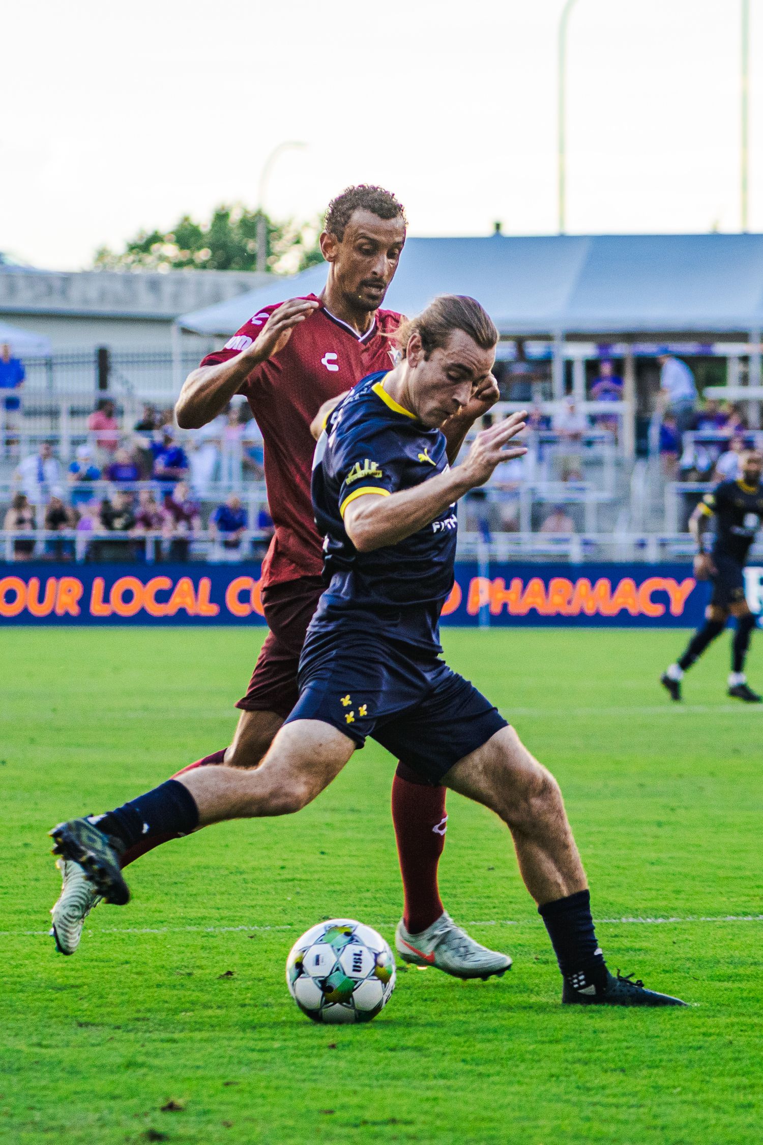 Soccer players competing for the ball during an intense match on a grass field with advertising boards visible.
