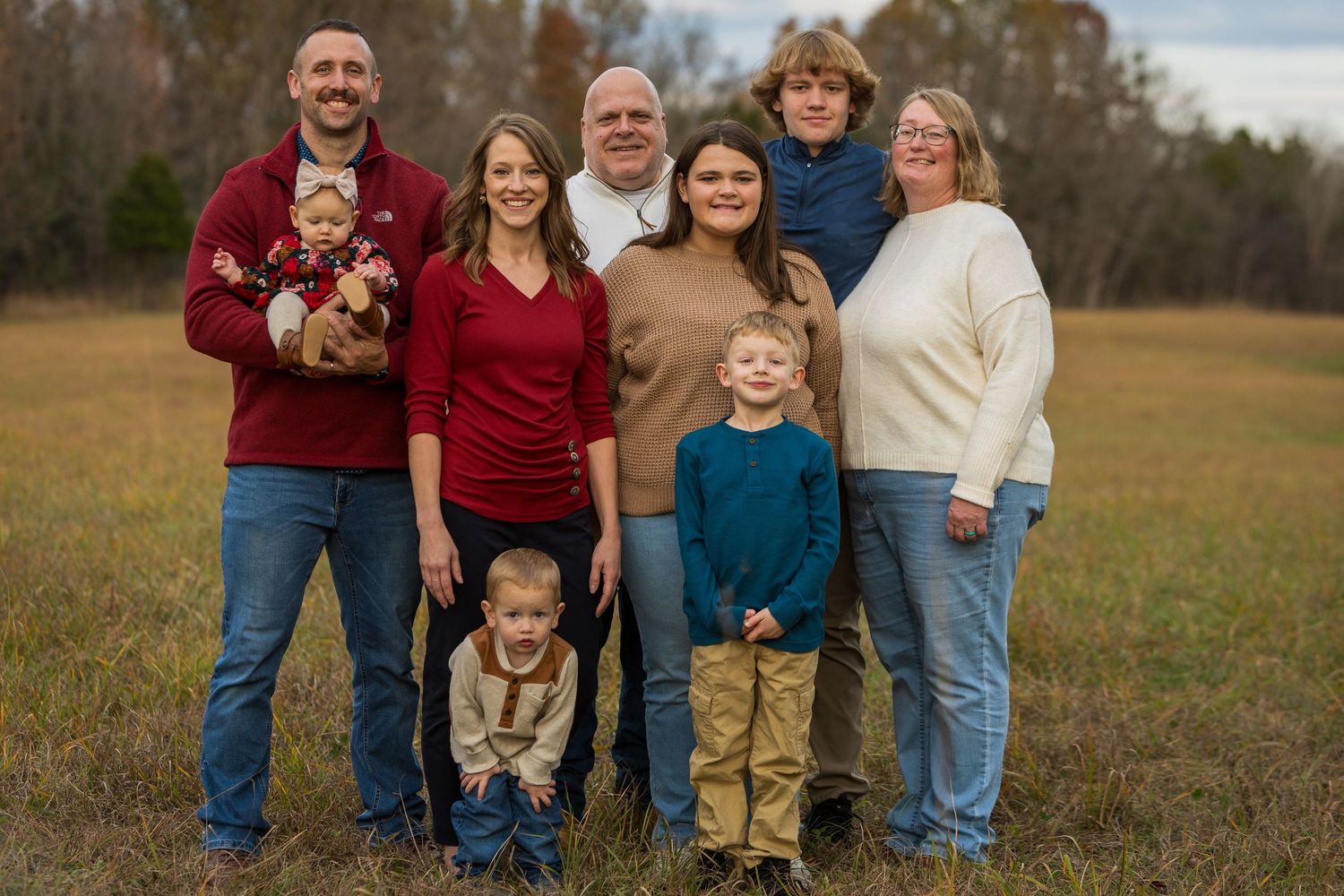 Multi-generational family group portrait outdoors in coordinated autumn outfits.