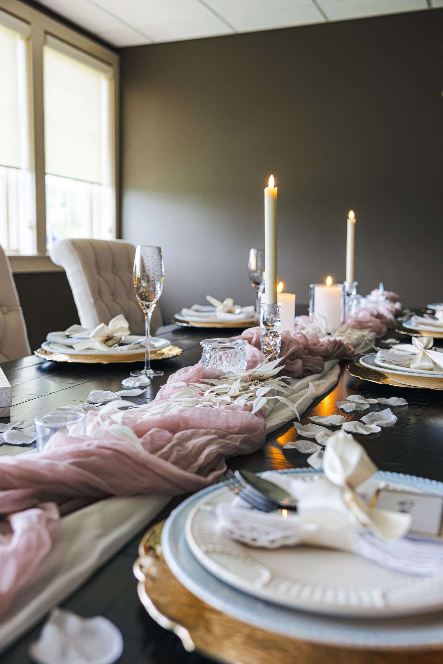 Elegant dining table set with candles, pink gauze runner, gold chargers, and white plates for a formal occasion.