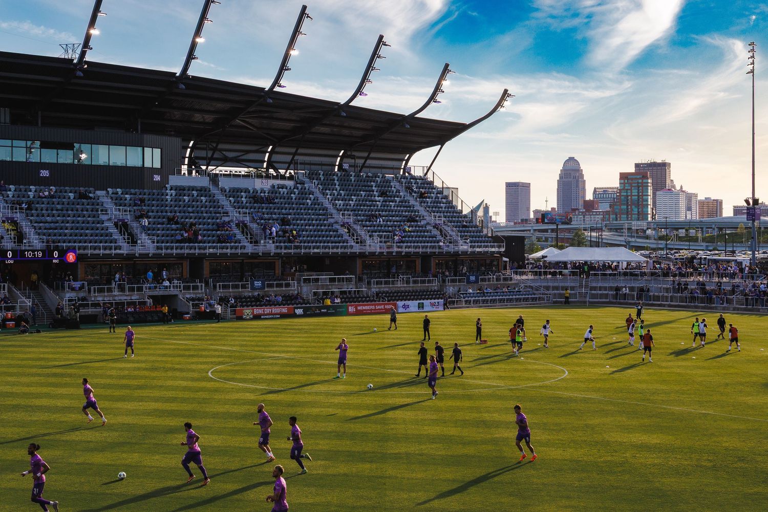 Soccer stadium with downtown skyline visible at sunset during match.