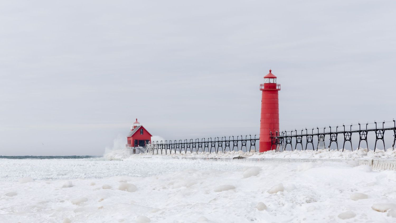 Two red lighthouses stand on a snow covered pier in winter landscape.