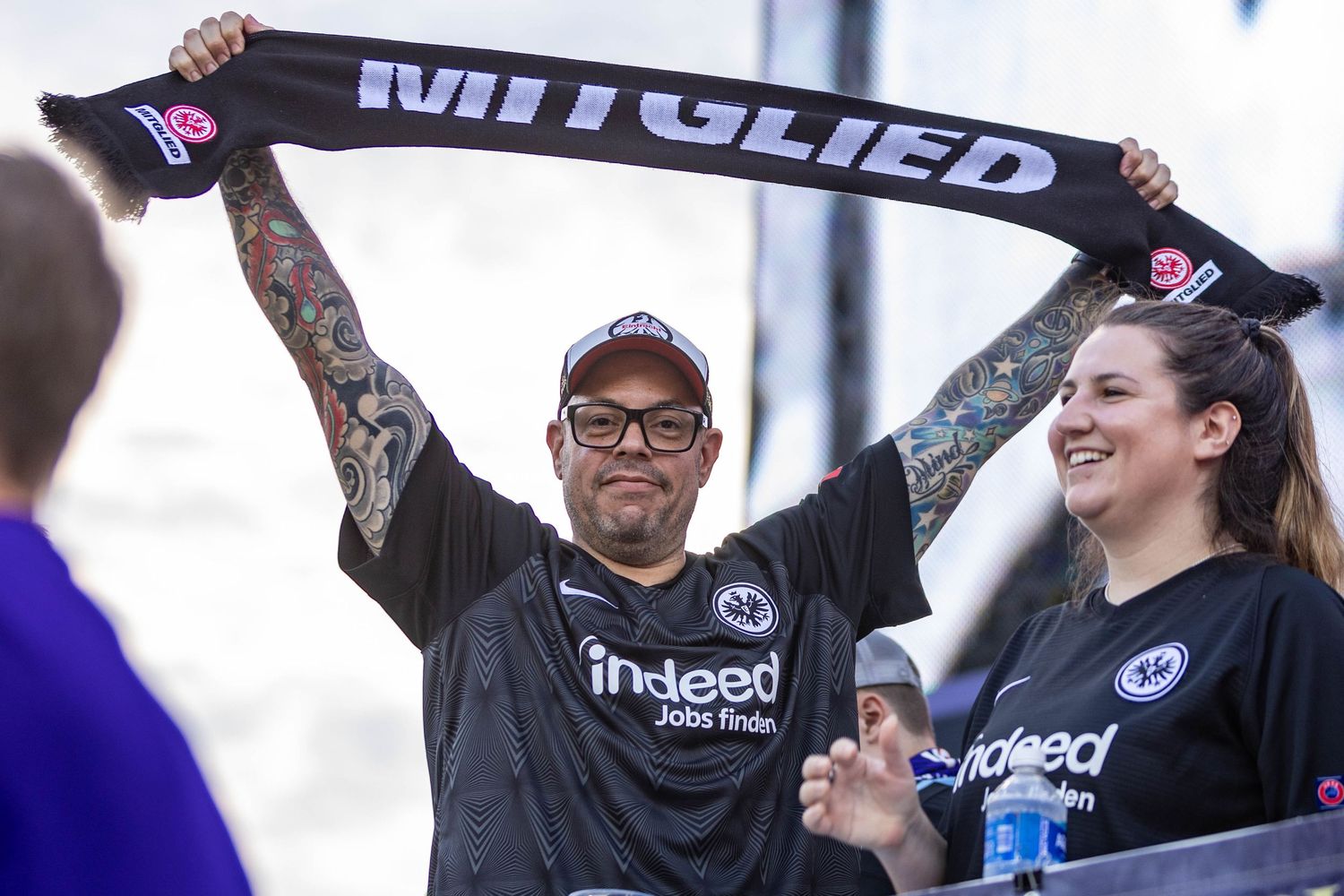 A dedicated sports fan holds up a black scarf showing team pride at a stadium.