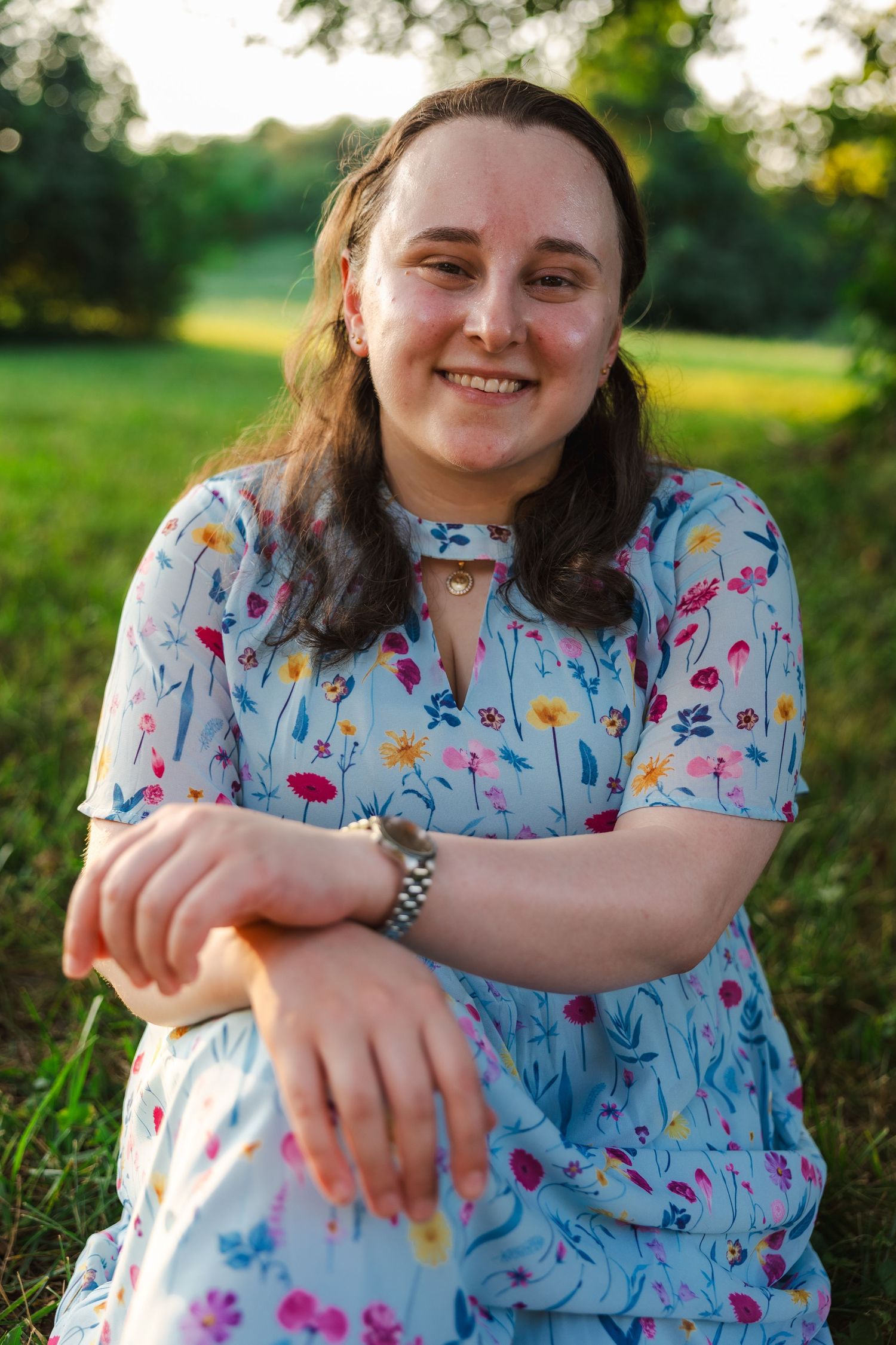 A person in a floral print top sits outdoors in a grassy field during golden hour.
