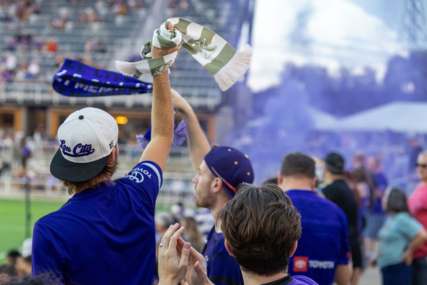 Baseball fans in blue jerseys celebrate and cheer in the stadium stands during an exciting game moment.
