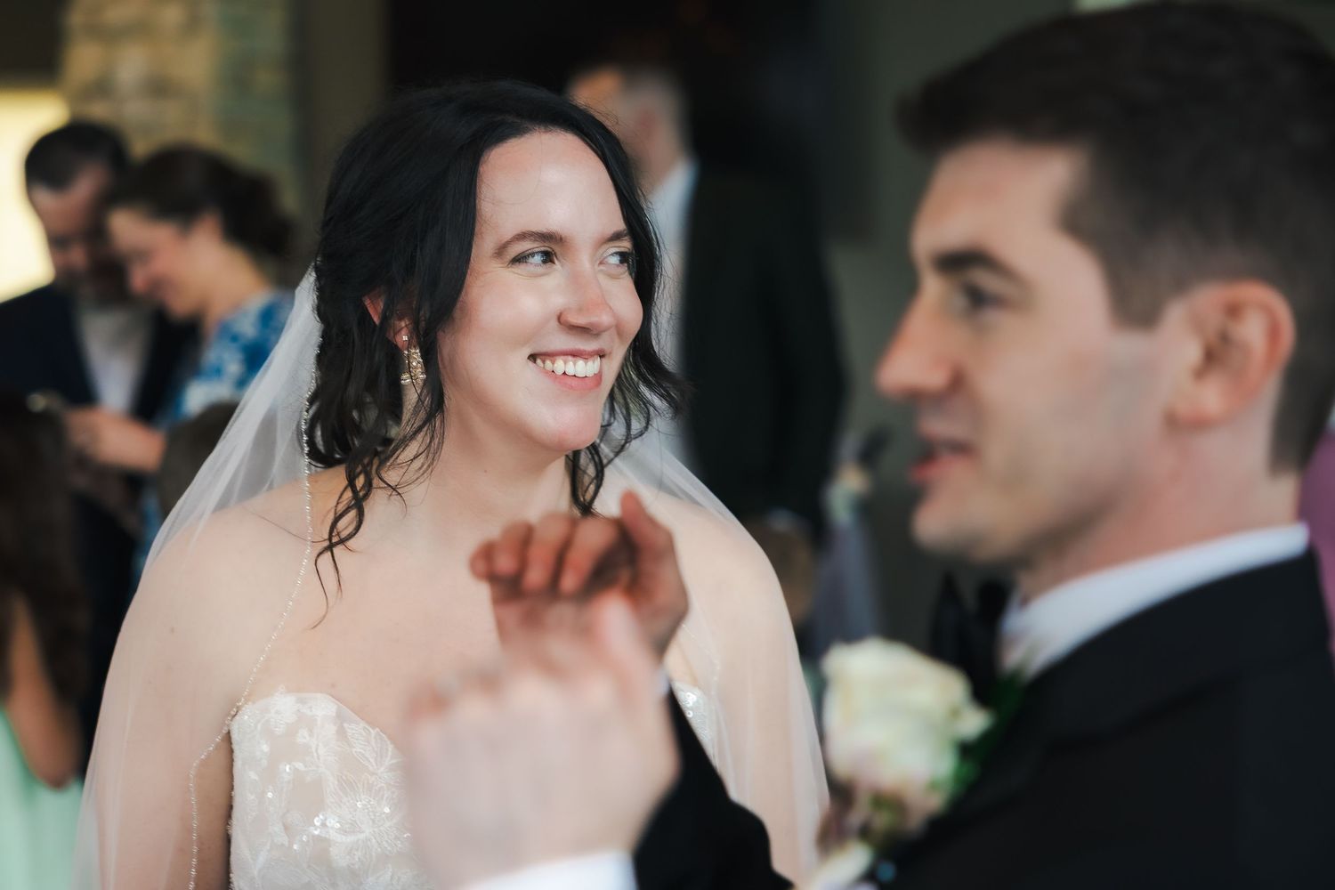 Bride in white gown and veil smiling at groom in black suit during wedding reception dance.