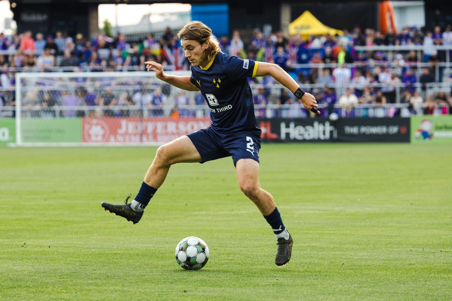 Louisville City soccer player Aiden McFadden in navy blue uniform dribbles ball on professional pitch during competitive match.
