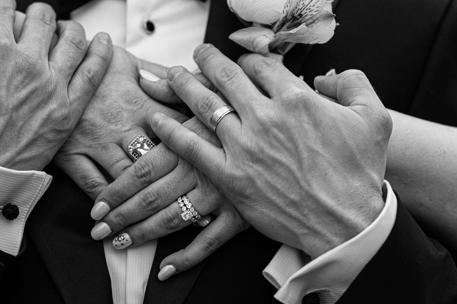 Black and white photo of wedding couple showing off their rings with hands stacked together.