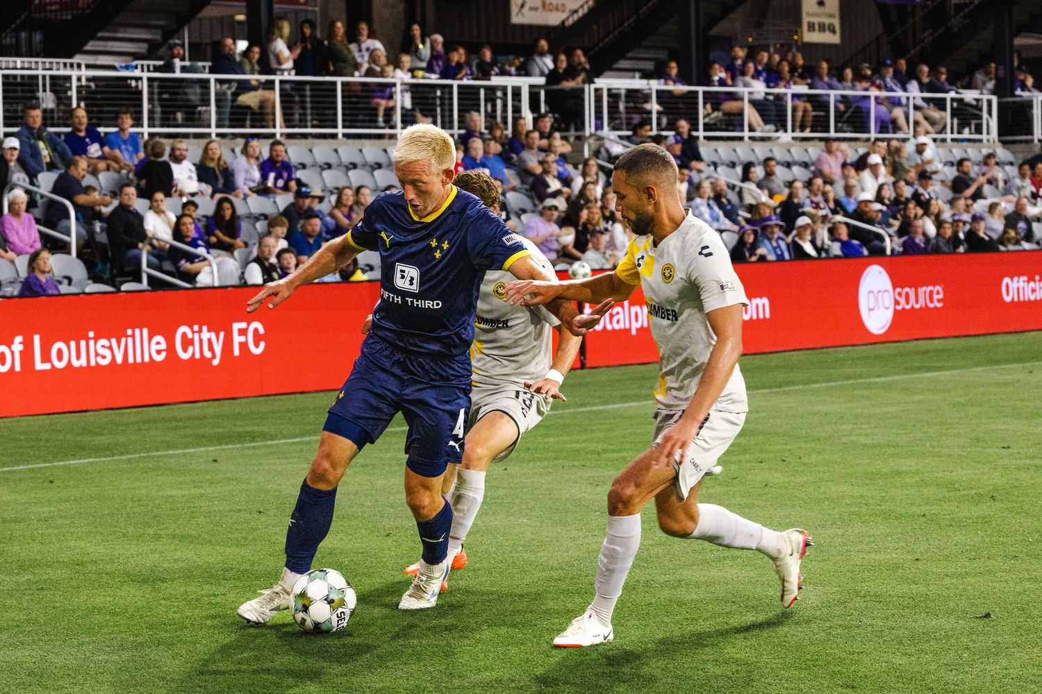 Soccer players from opposing teams battle for possession of the ball during a match at Louisville City FC stadium.