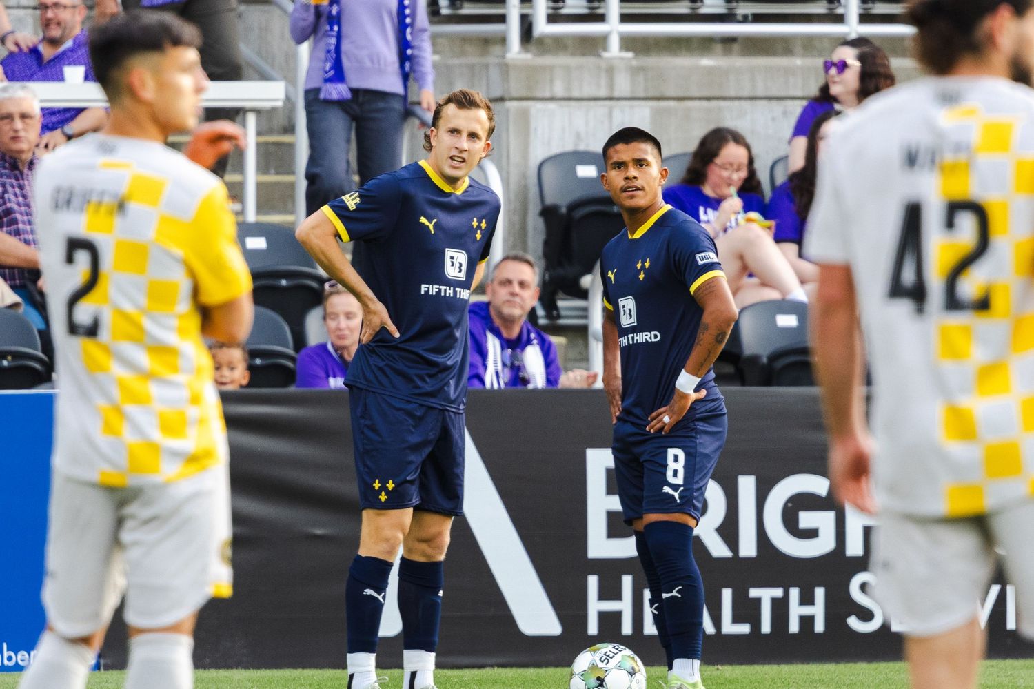 Soccer players in navy and checkered uniforms standing on field during match.