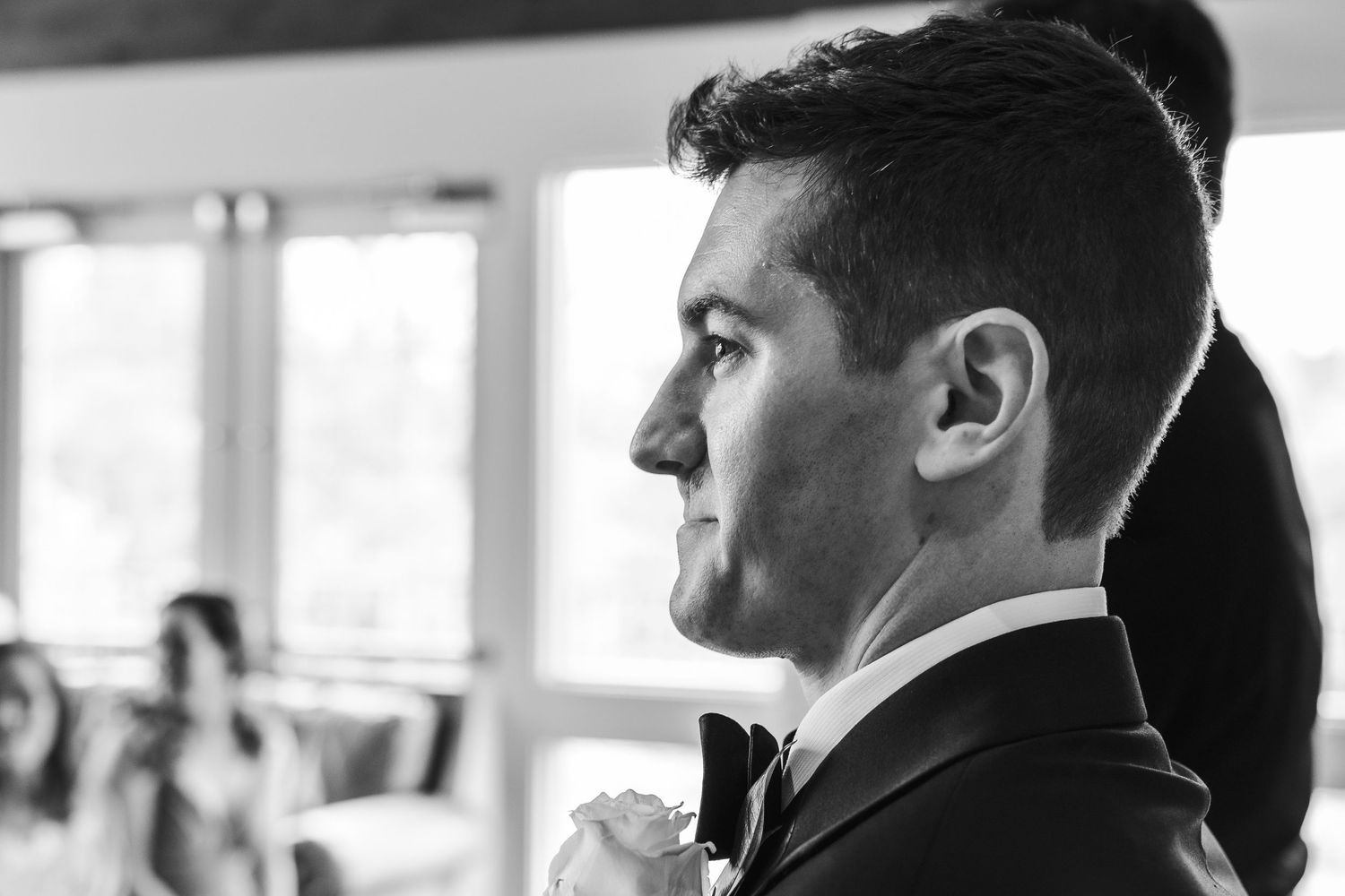 Black and white portrait of a groom in a tuxedo smiling at his wedding ceremony.