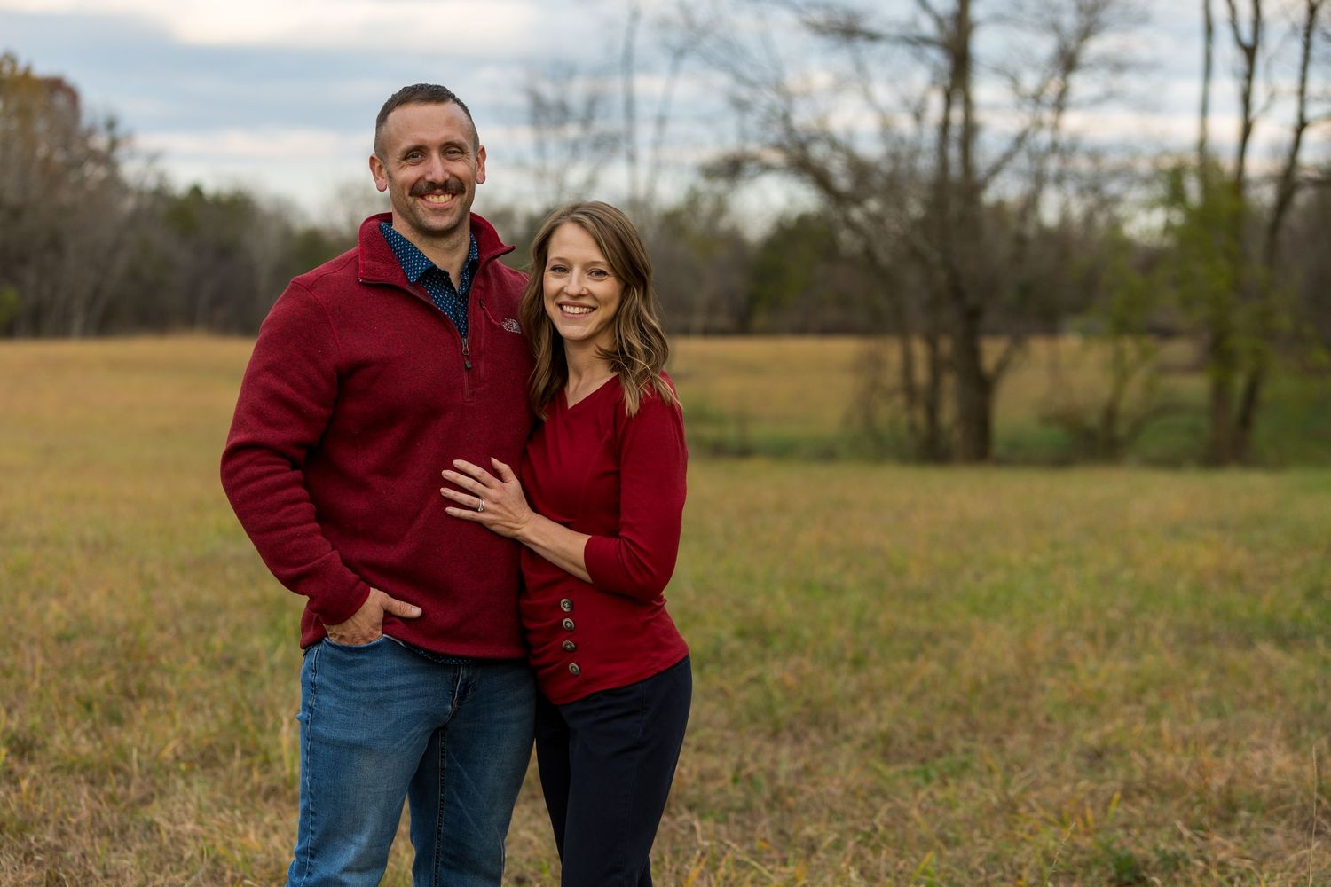 Happy couple in matching red sweaters posing together in fall field.