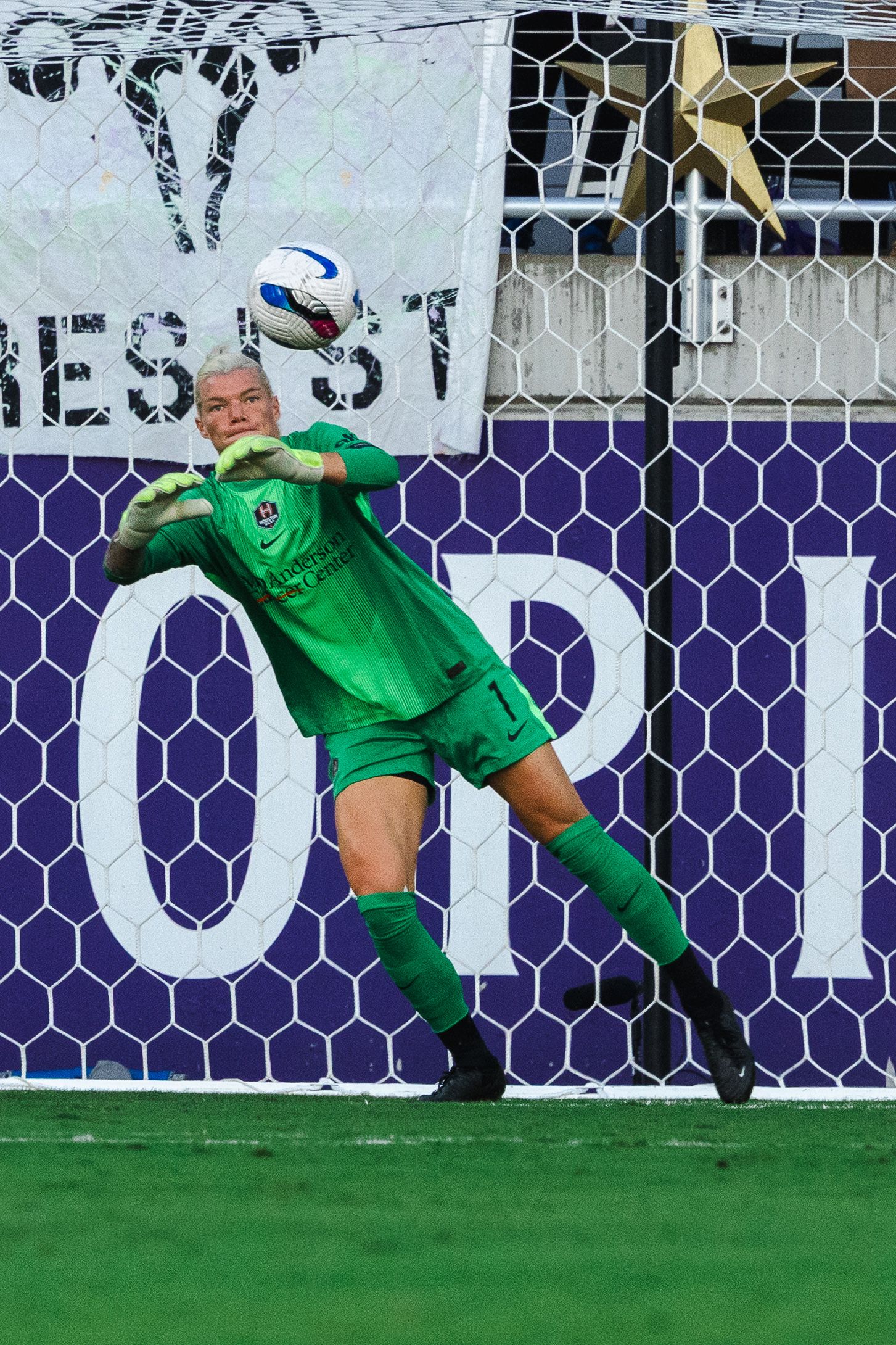 A goalkeeper in green uniform makes a diving save during a soccer match.