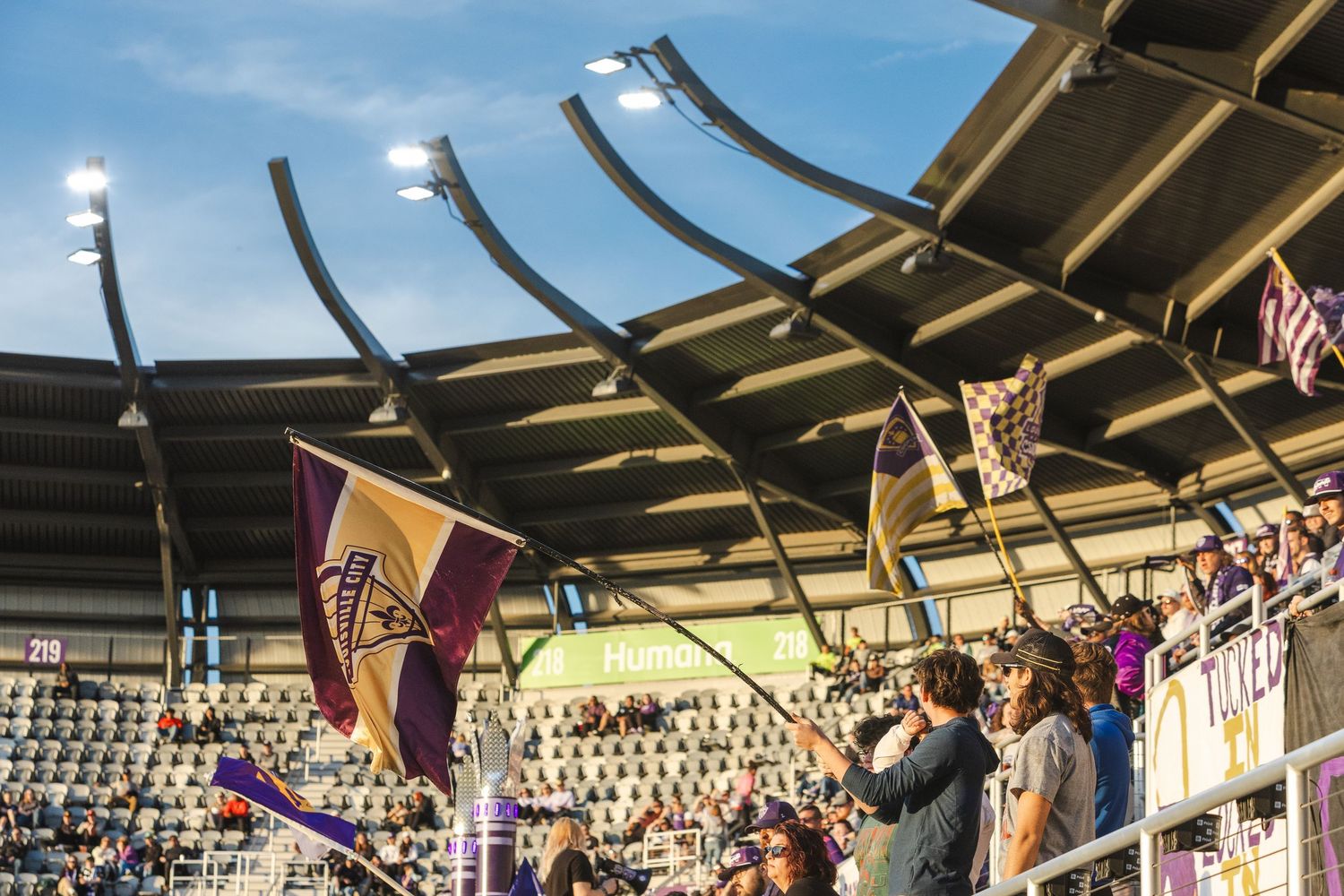 Stadium architecture with flags and lighting fixtures visible against a bright blue sky.