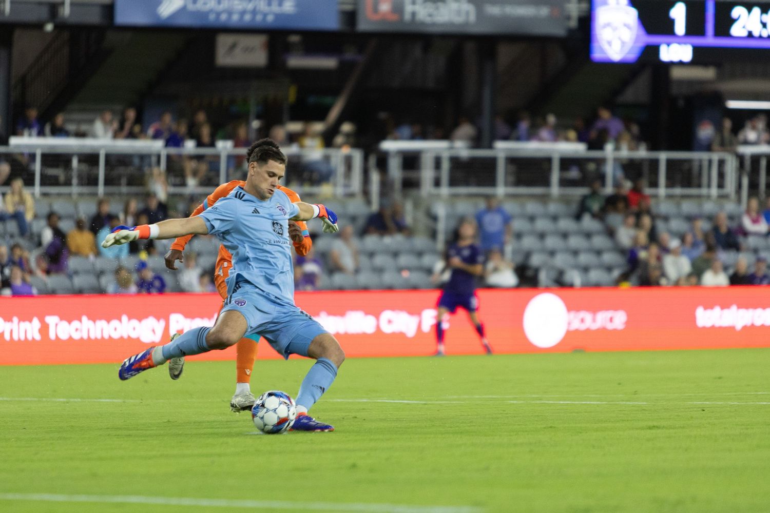 Soccer player in light blue uniform prepares to kick ball during evening match.