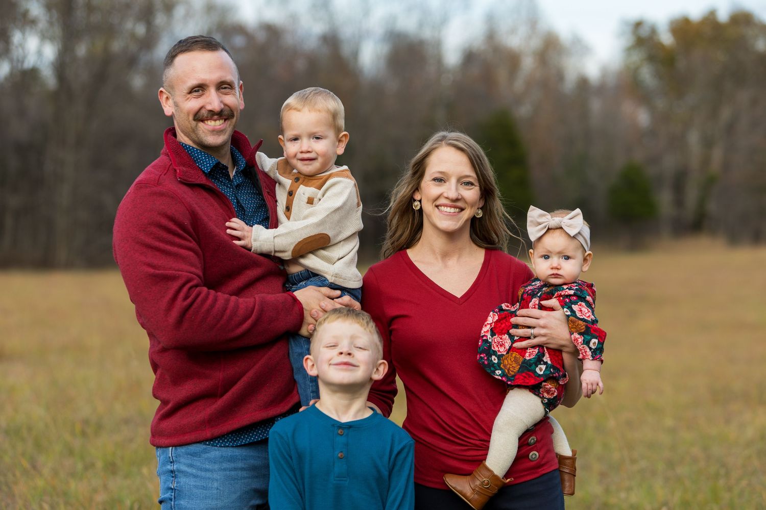 Family of four in coordinating red sweaters posing together in autumn field.