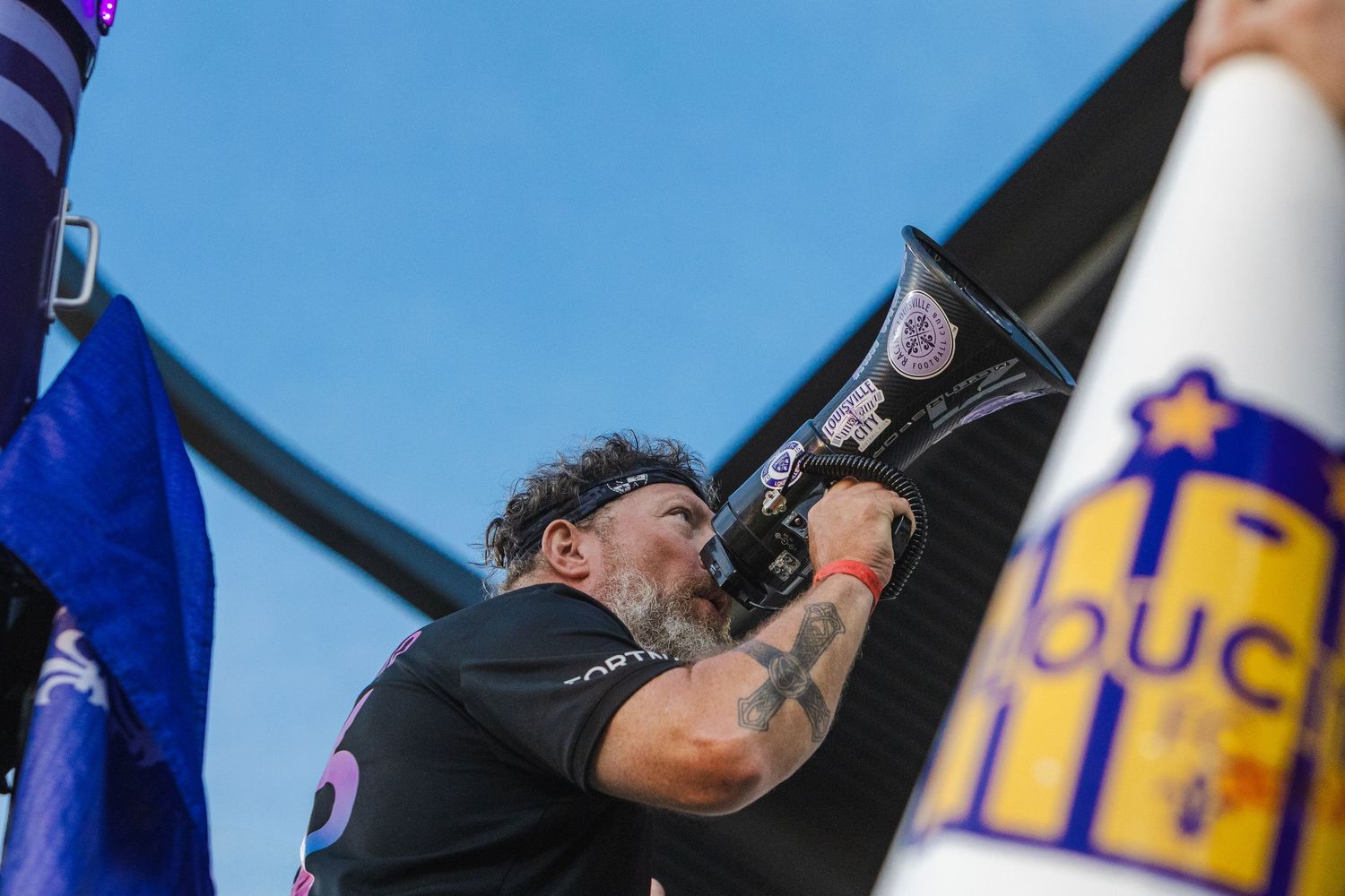 Fan with tattoos cheers while holding a flag at a soccer match.