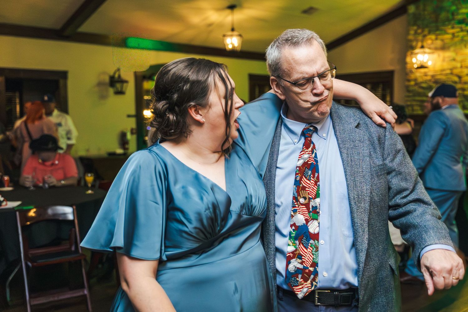 Wedding reception scene with guests in blue attire dancing and celebrating under warm lighting.