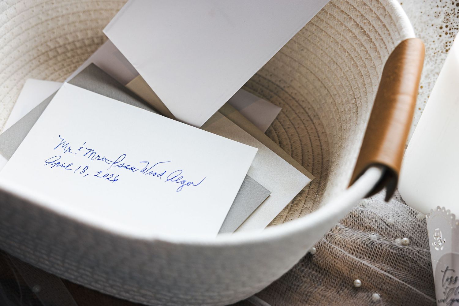 Wedding envelopes with handwritten calligraphy addresses sit in a white rope basket, ready for mailing.