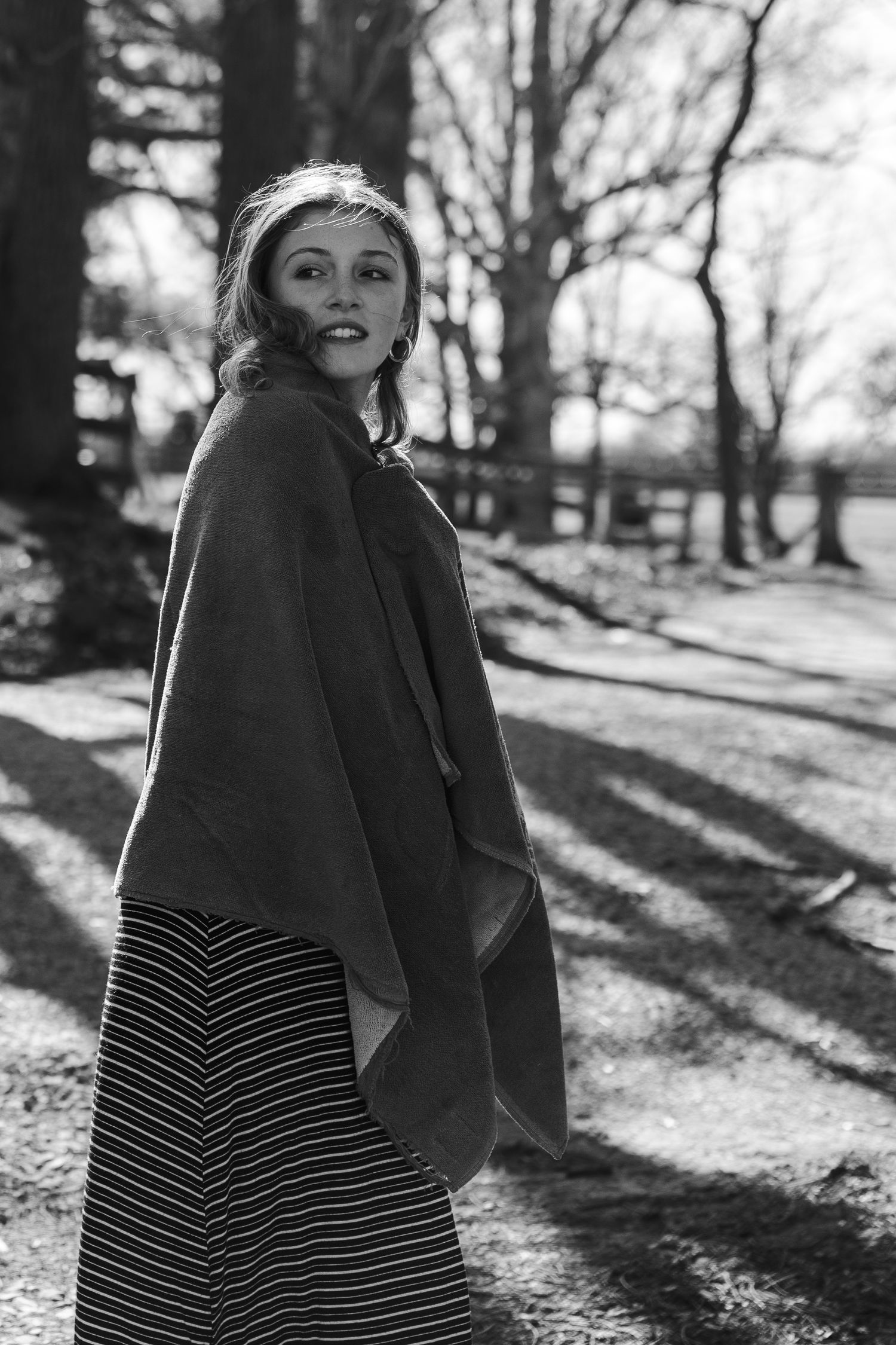 Black and white portrait of person in winter coat and striped dress outdoors with dramatic shadows.