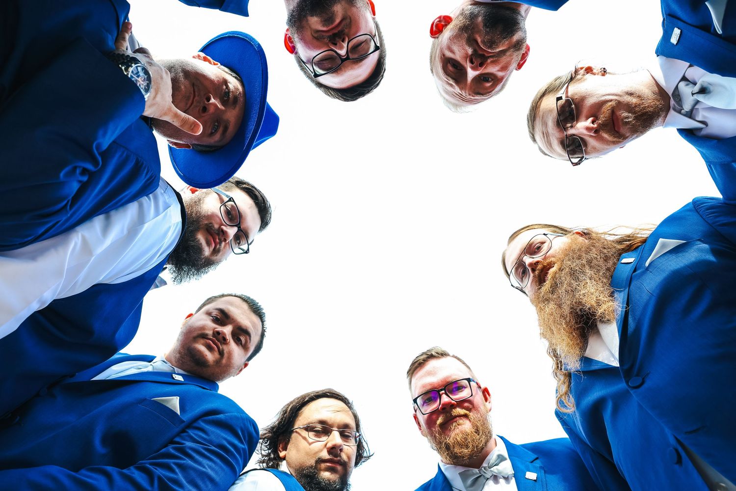 Baseball players in blue jerseys form a circular huddle viewed from below against a white sky.