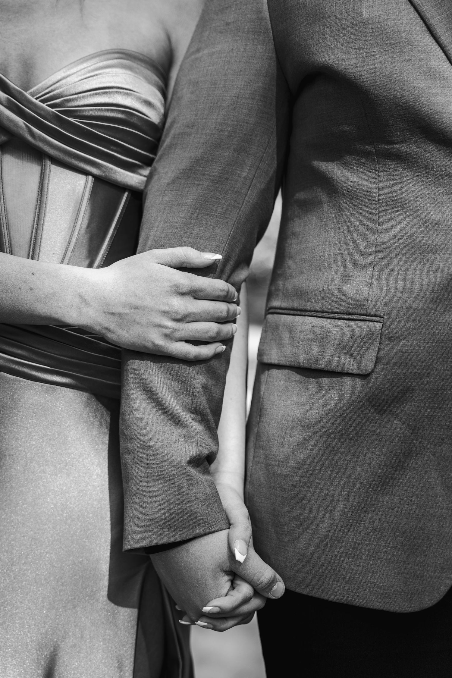 Black and white close-up of a couple's formal attire and embracing hands.