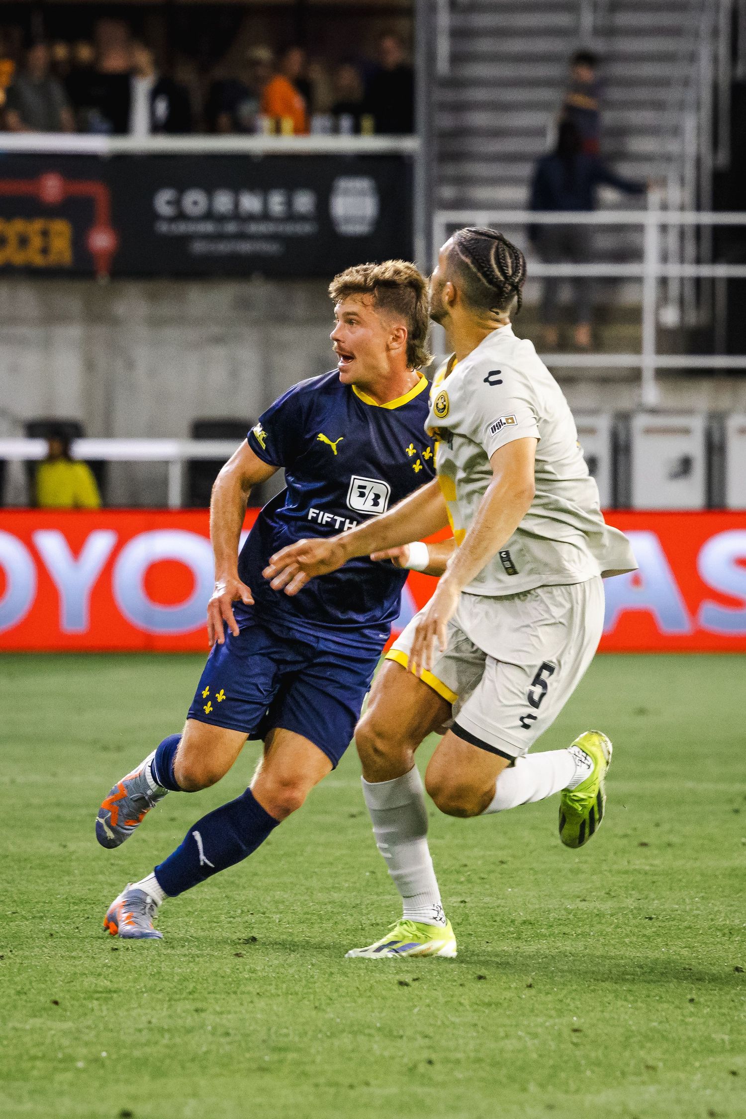 Two soccer players competing for ball during match under stadium lights.