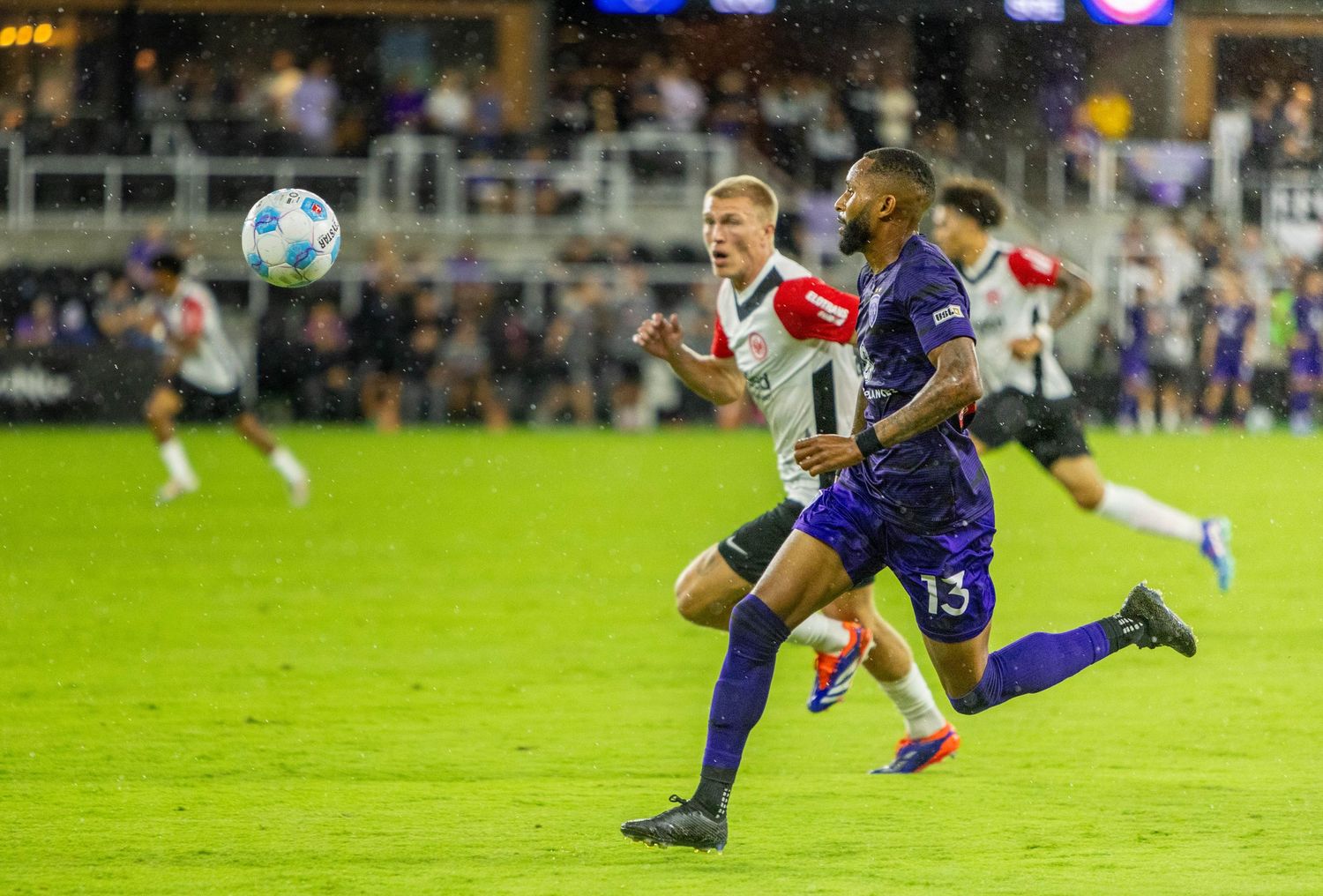 Soccer players from opposing teams chase after the ball during intense match action.