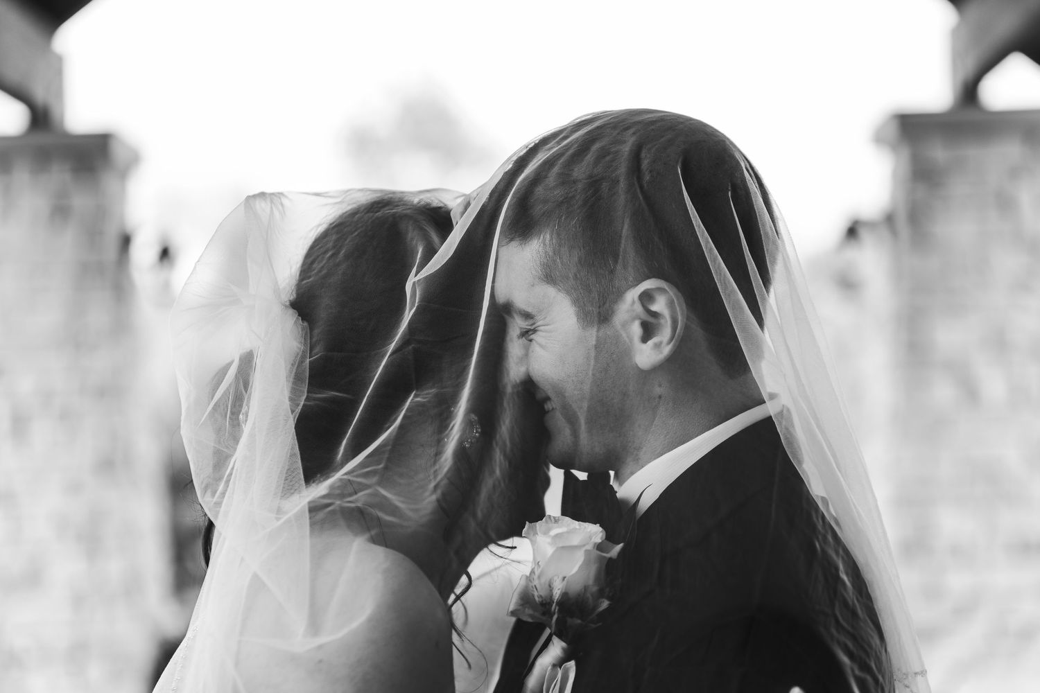 Bride and groom sharing an intimate moment under a wedding veil in a romantic black and white photo.