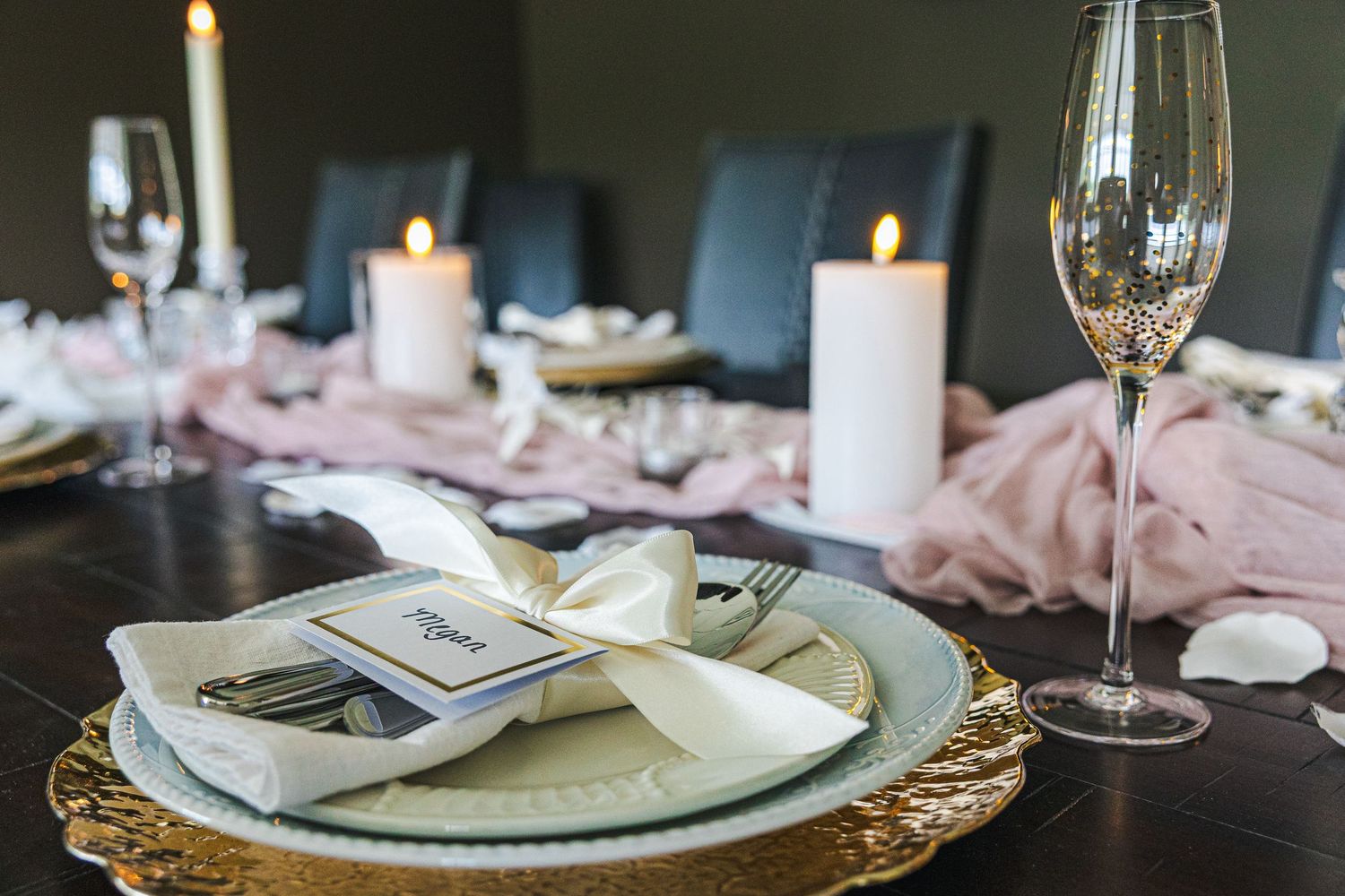 Elegant wedding table setting with gold charger plates, white candles, champagne flutes, and blush pink fabric runner.