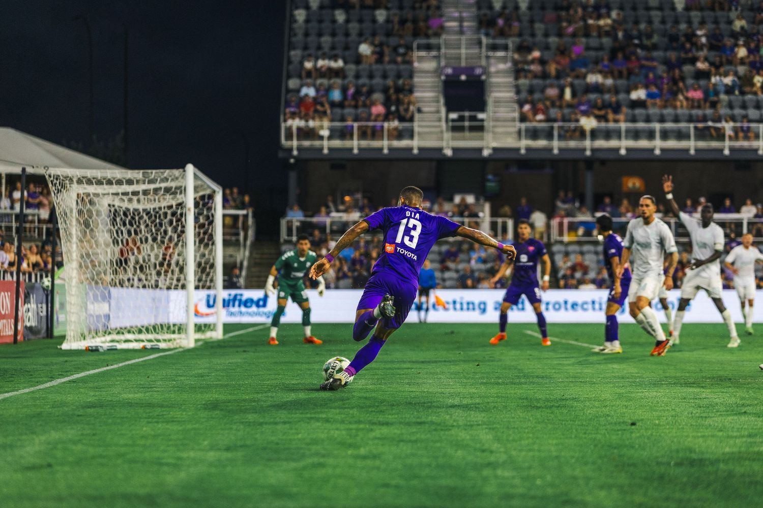 Soccer player takes a shot on goal during an intense match with goalkeeper diving to make the save.
