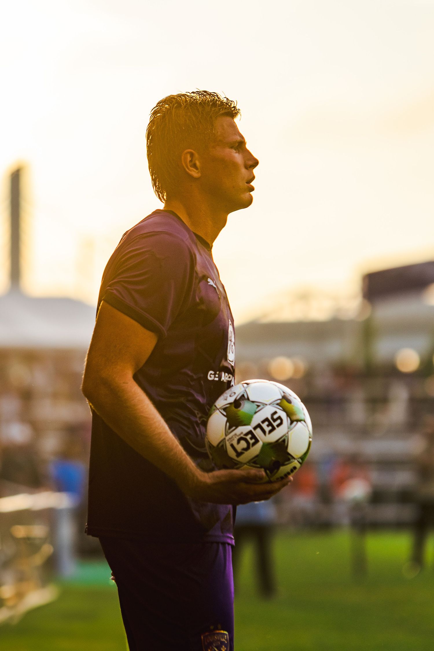 Rugby player in purple jersey holds ball during sunset training session at sports field.