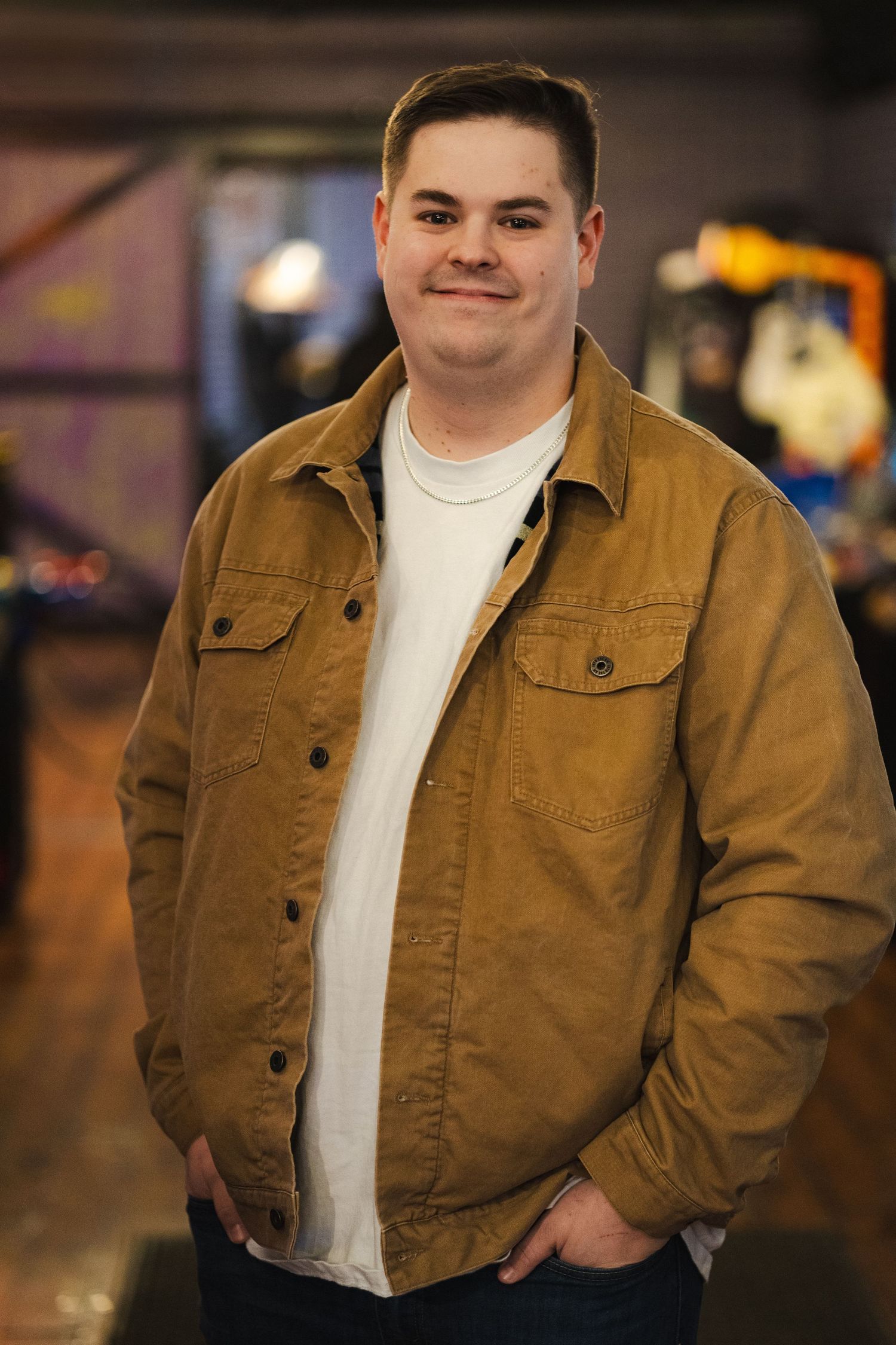 Casual portrait of a person wearing a brown jacket and white t-shirt in an indoor setting.