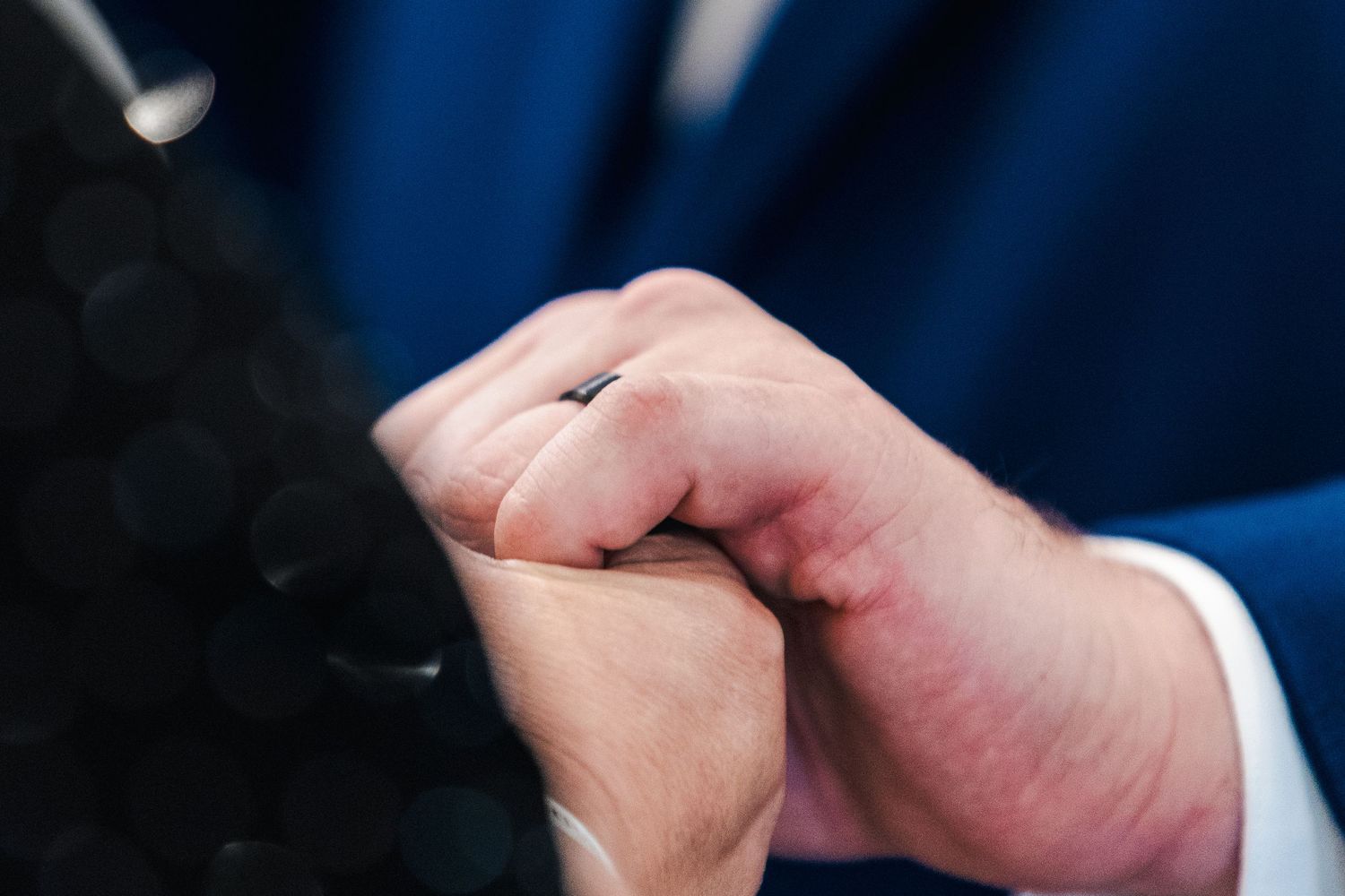 Two hands tenderly clasped together in an intimate moment against a dark blue background.