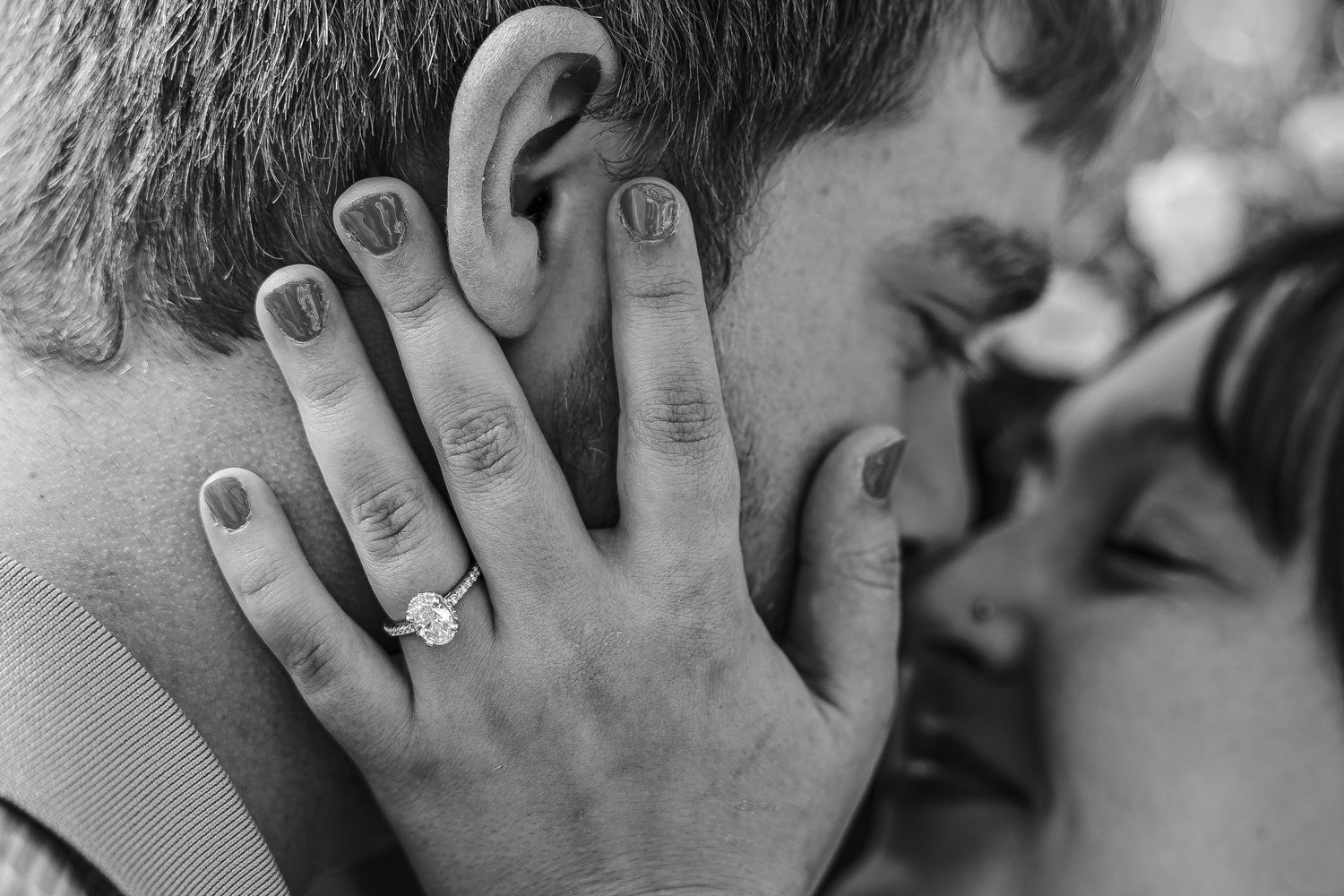 Black and white photo of couple almost kissing, woman's hand on man's face showing diamond engagement ring.