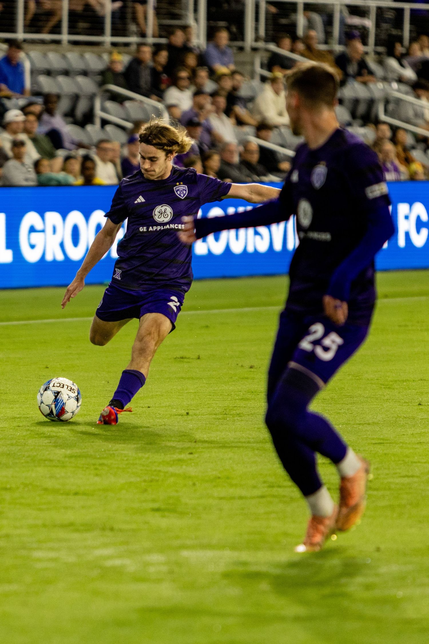 Players in purple jerseys coordinate passing play during nighttime soccer match.