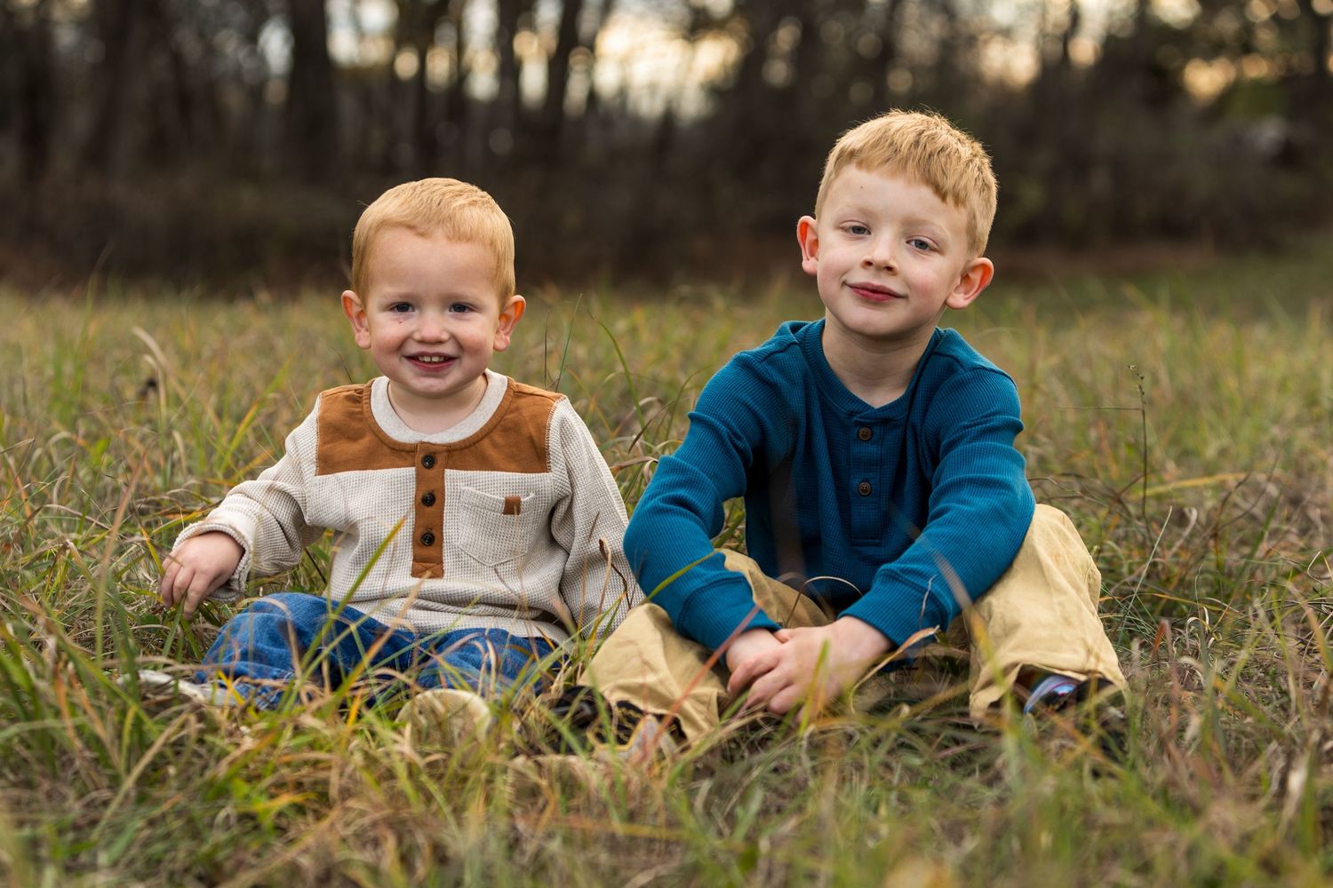 Two young boys sitting together in tall grass during golden hour.