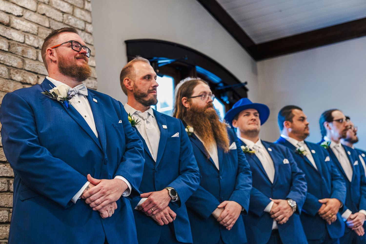 A line of groomsmen in matching navy blue suits stand together during a wedding ceremony.
