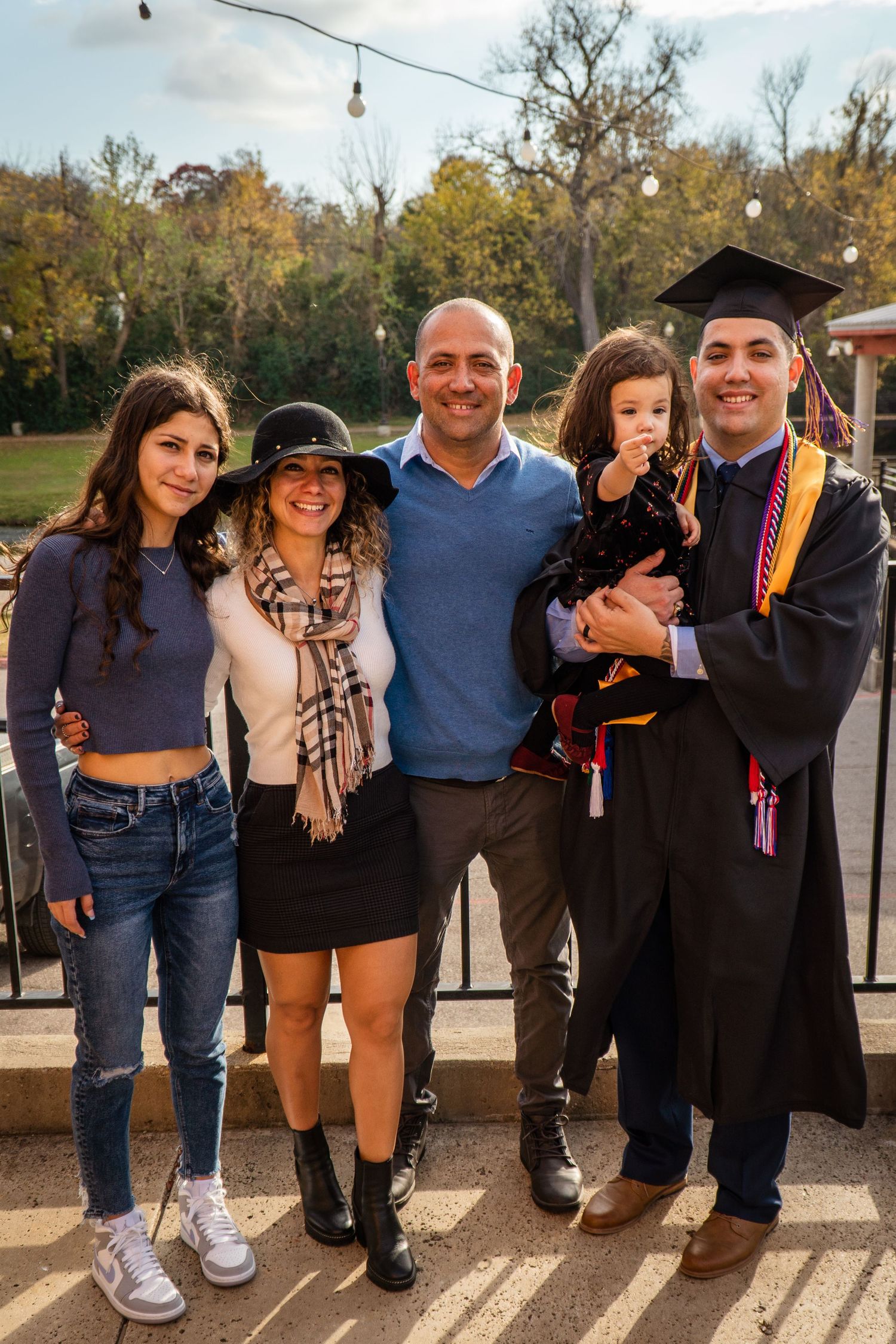 A group of people stand together outdoors on a sunny day celebrating a graduation ceremony.