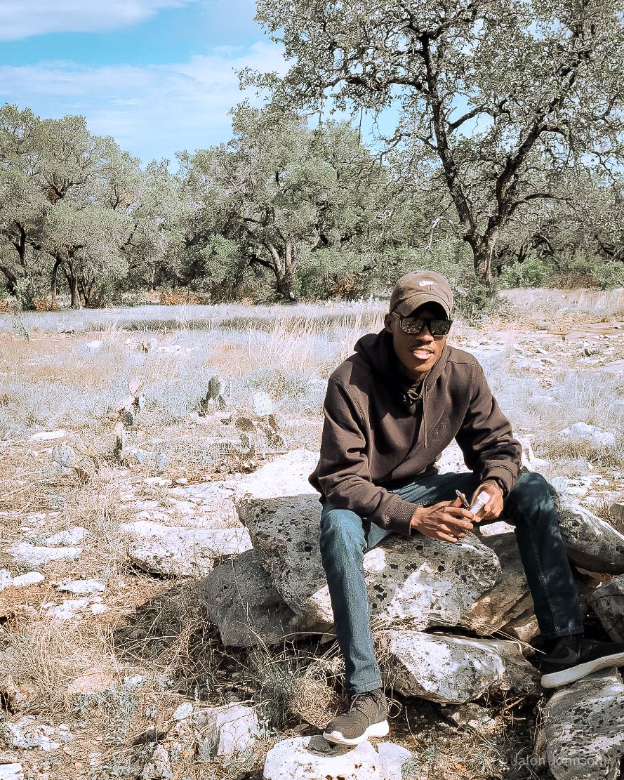 Person in brown jacket sits on rocky terrain in a desert landscape.