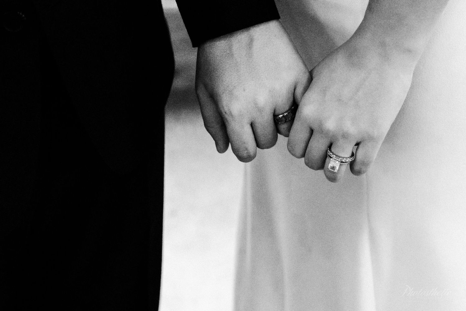 Black and white close-up of two people holding hands, showing wedding and engagement rings.