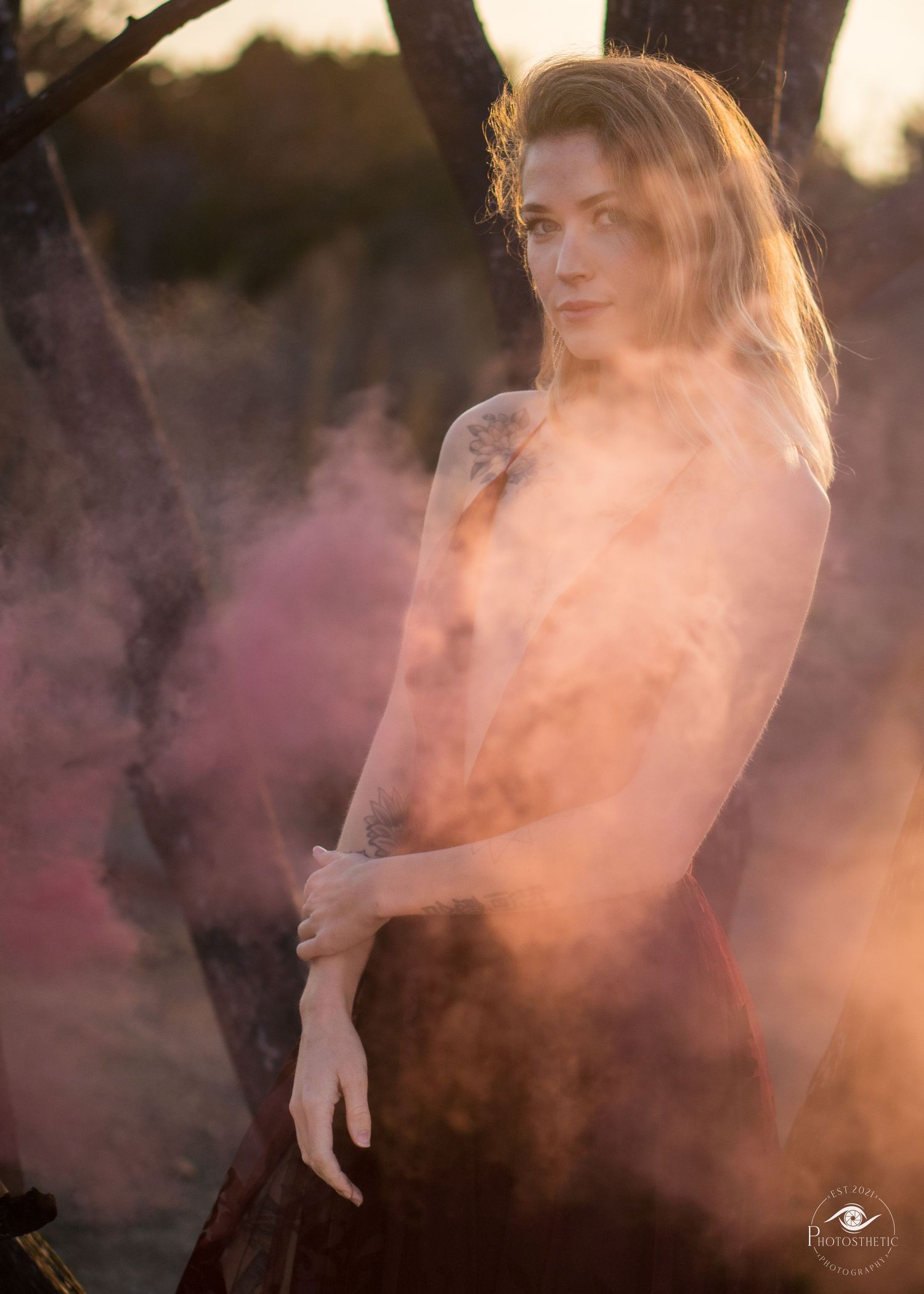 Artistic black and white outdoor portrait of a tattooed woman in an elegant dress with atmospheric smoke.