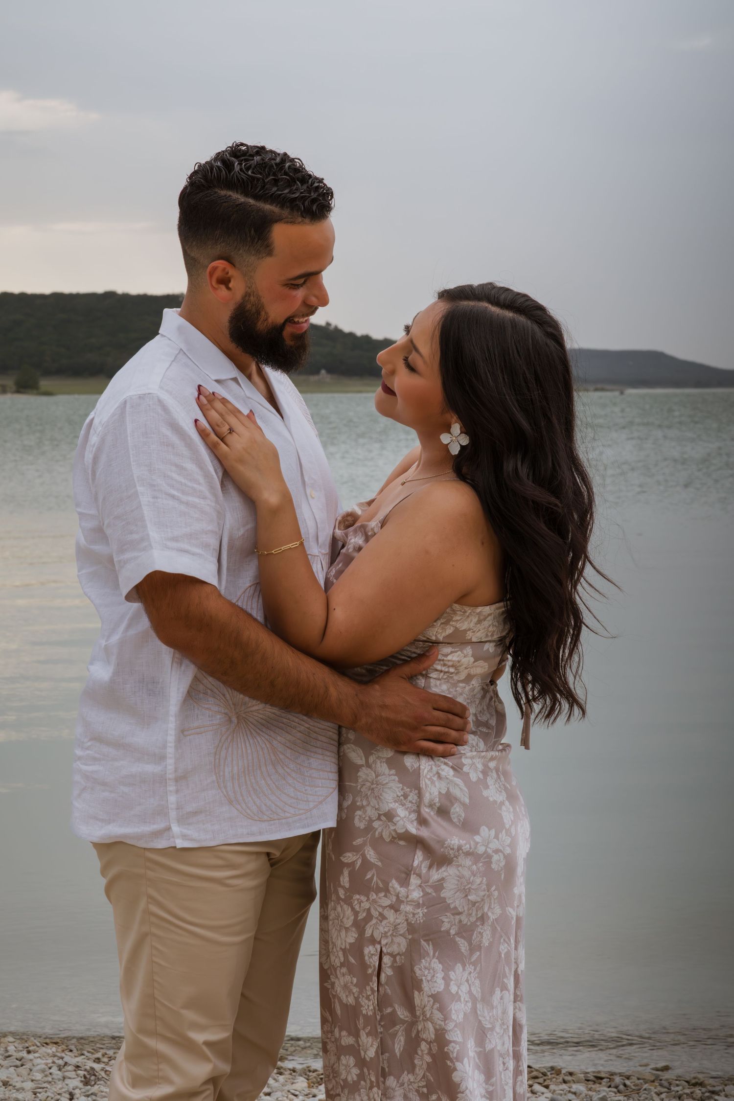 Couple embracing and gazing at each other near lakeside in coordinated beach engagement photos.