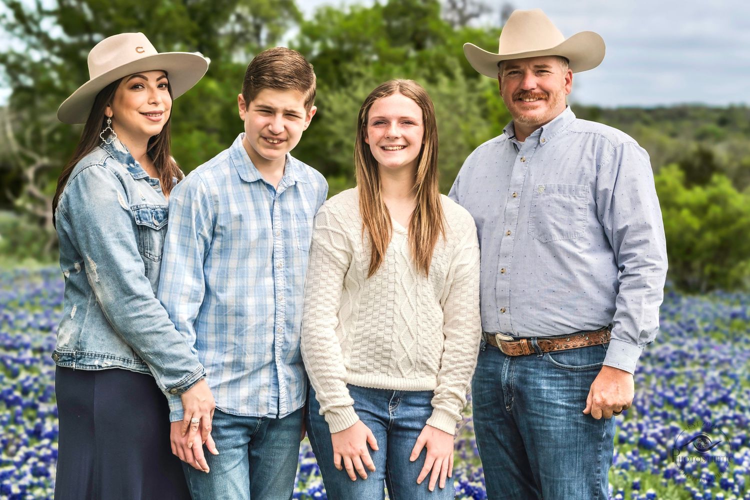 Family of four standing together in a bluebonnet field during a spring outdoor portrait session.