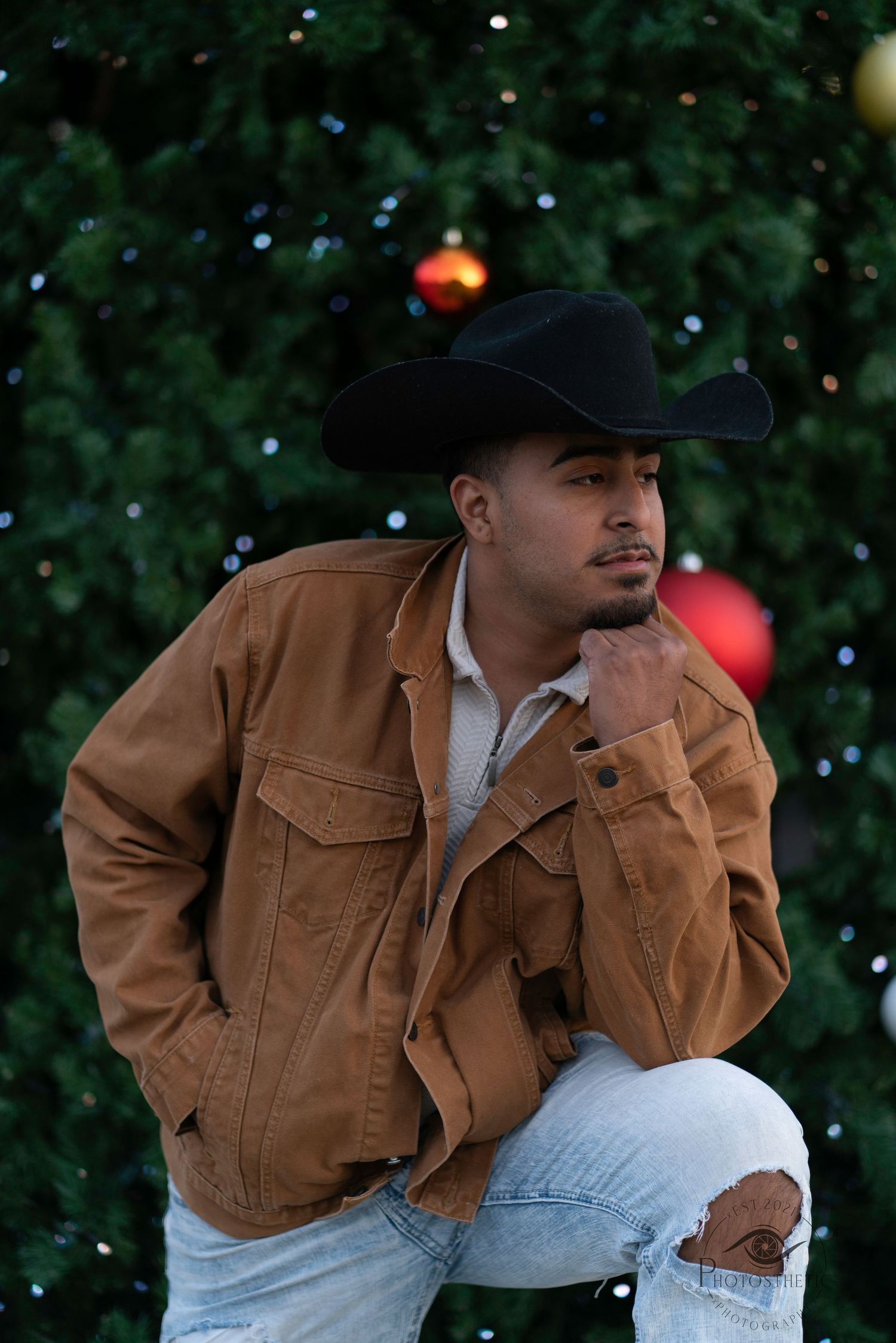 Man in brown jacket and black cowboy hat poses against dark background with twinkling lights.