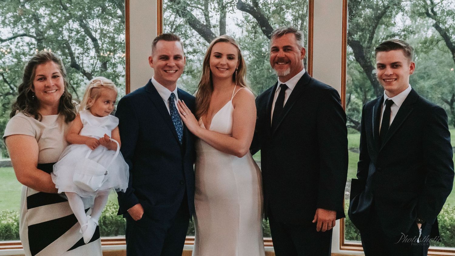 Family standing together indoors during a wedding, including the bride, groom, and relatives posing for a formal portrait.