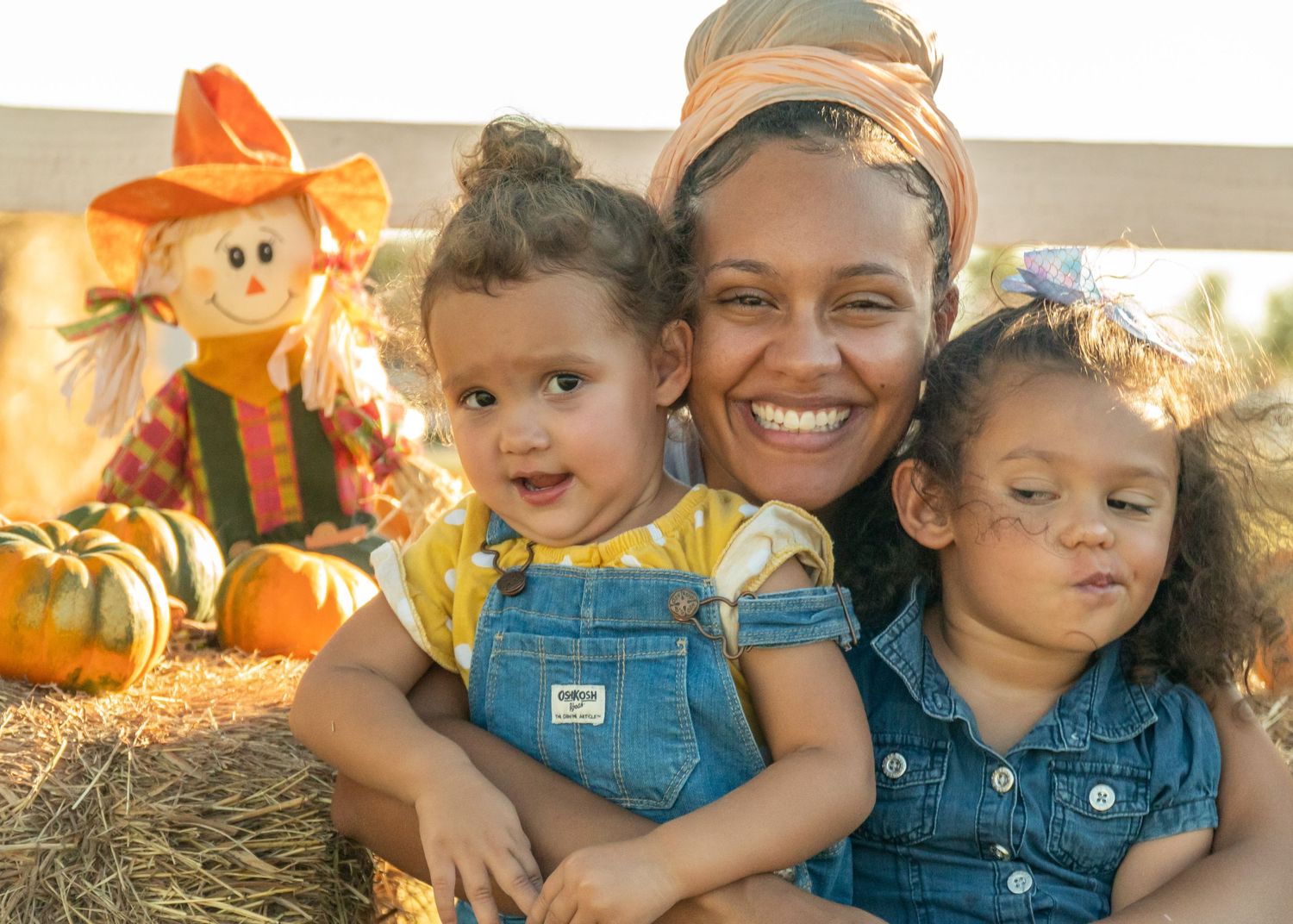 Outdoor fall family portrait of a mother and two children at a pumpkin patch in natural light.